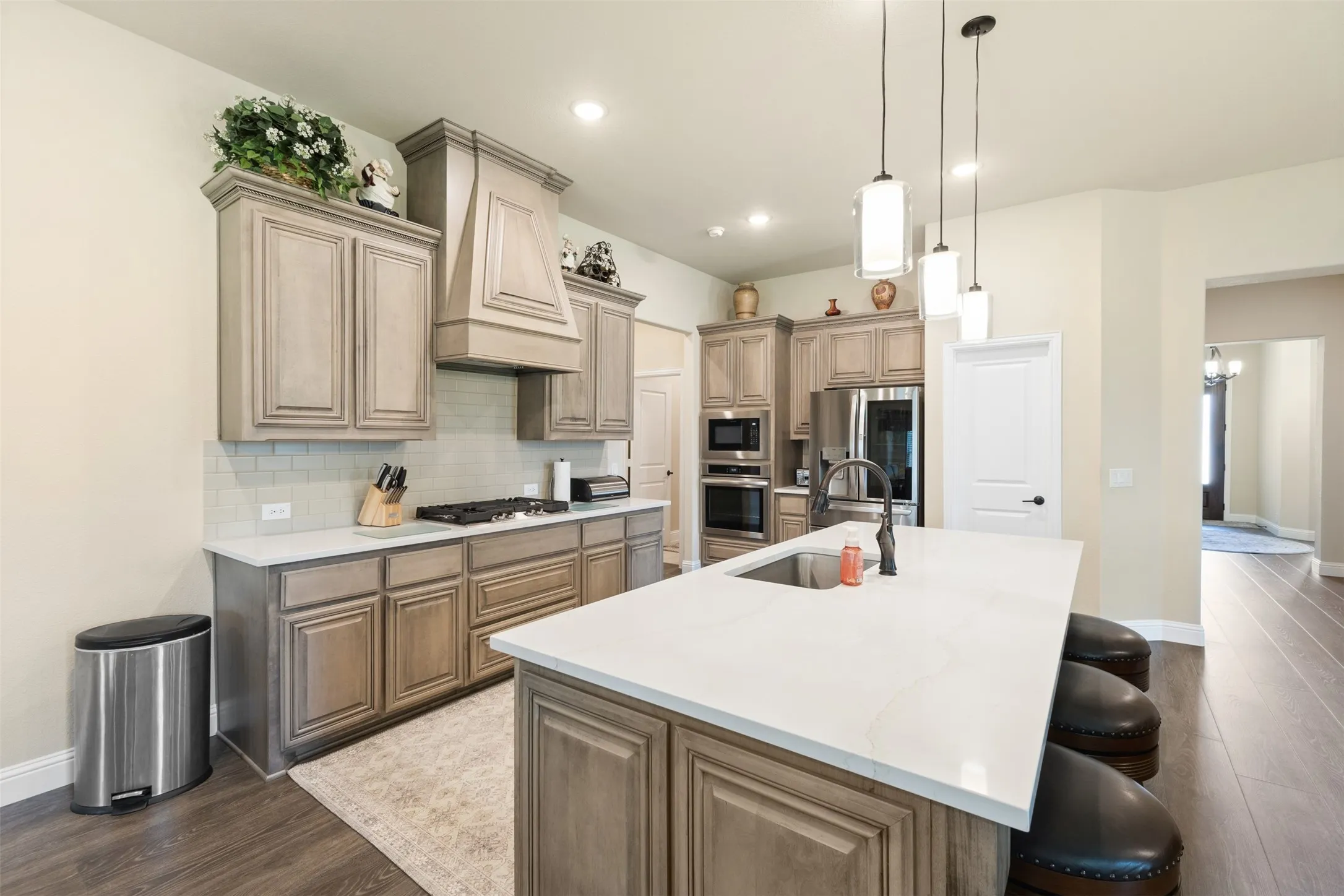Kitchen featuring an expansive center island with a built-in sink, pendant lighting, wood-finish flooring, light-toned cabinetry, and stainless steel appliances
