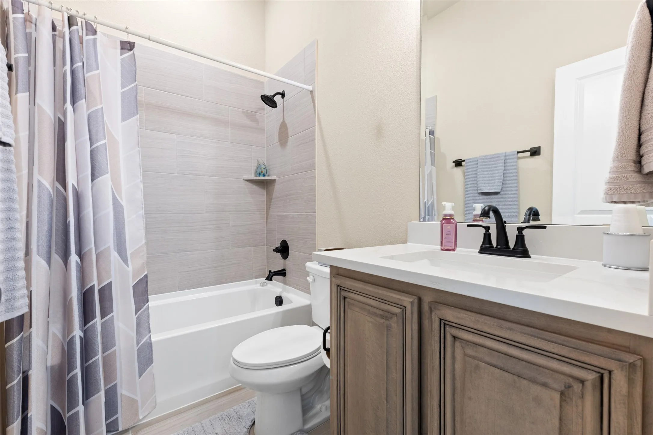 Bathroom featuring a built-in tub with a tile surround, matte black fixtures, a white vanity with shaker-style cabinetry, and a countertop with an integrated sink