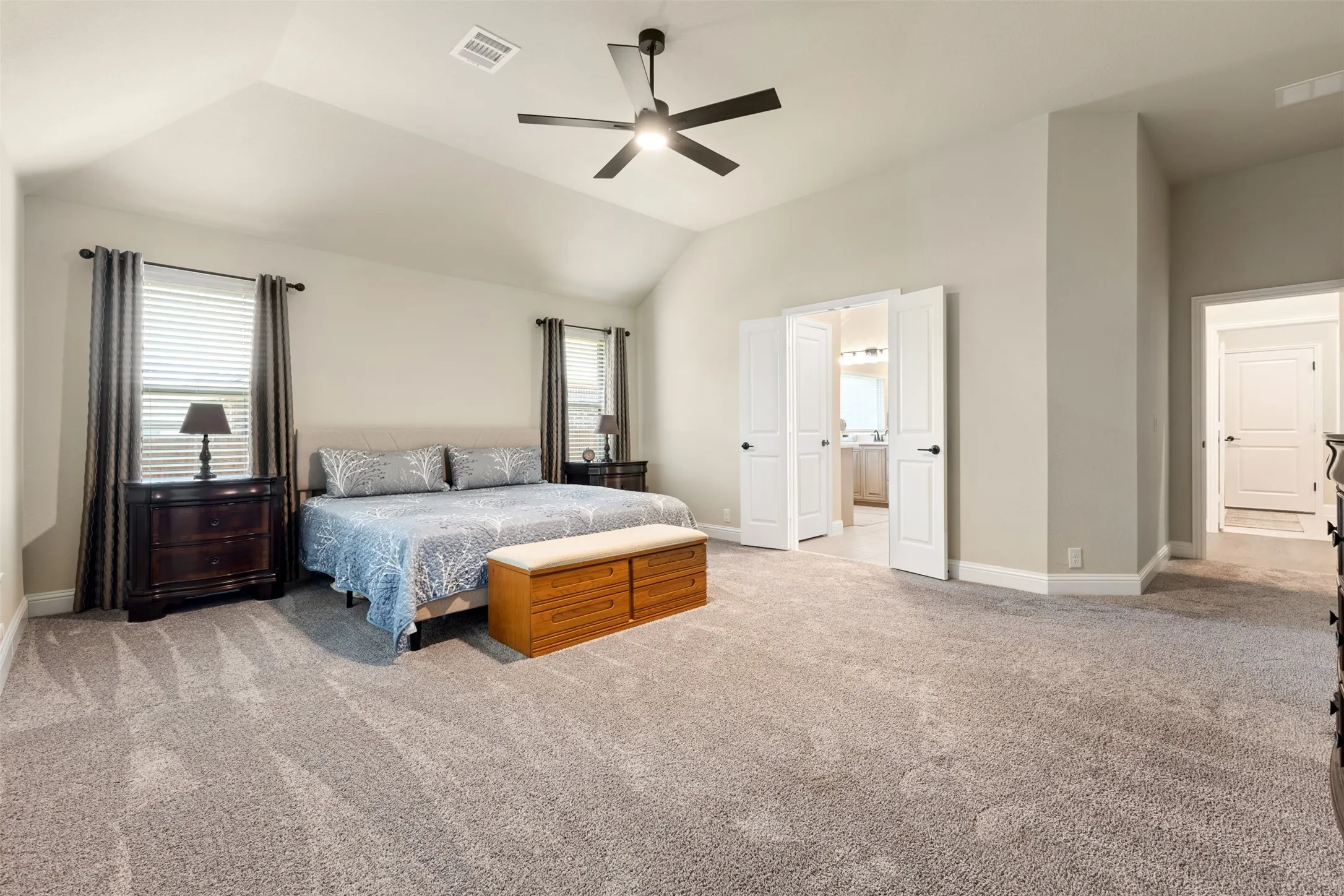 Vaulted ceiling room featuring light-toned walls, gray carpet flooring, and a ceiling fan