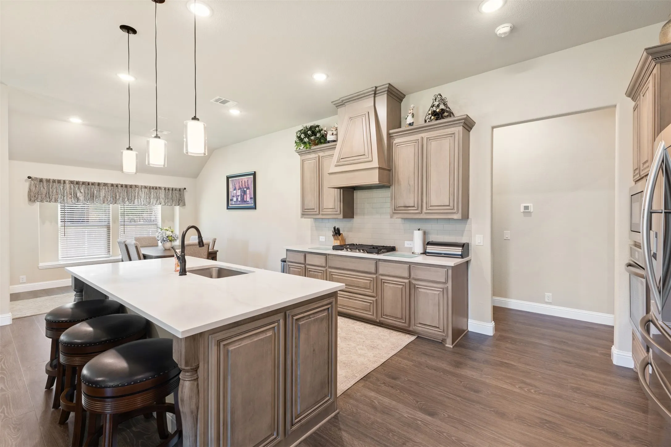 Kitchen featuring a central island with countertop seating, wood-finish flooring, recessed lighting, pendant lights, and a built-in oven and microwave