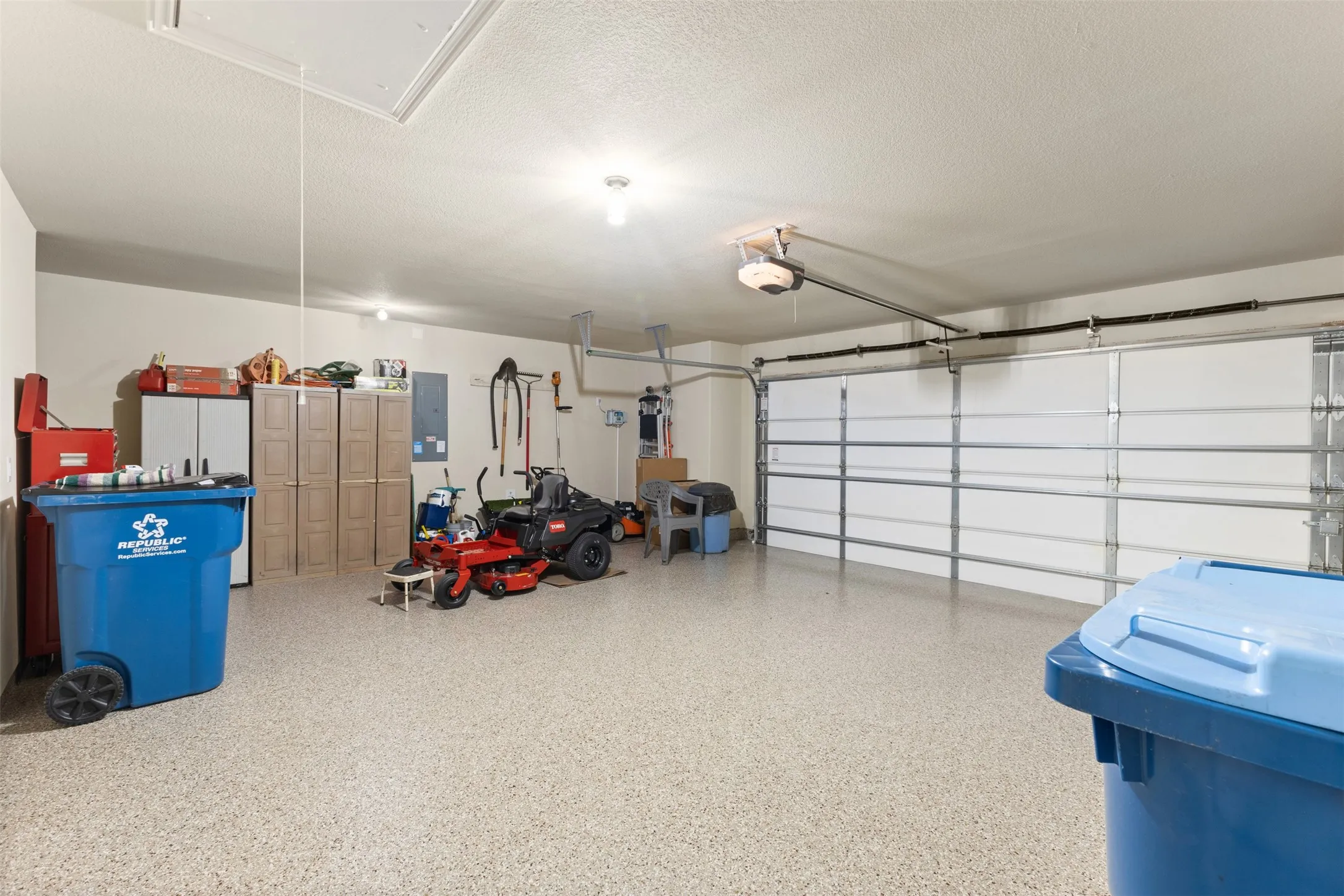 Spacious garage featuring a light-toned epoxy floor coating, two overhead garage doors, and an attic access panel