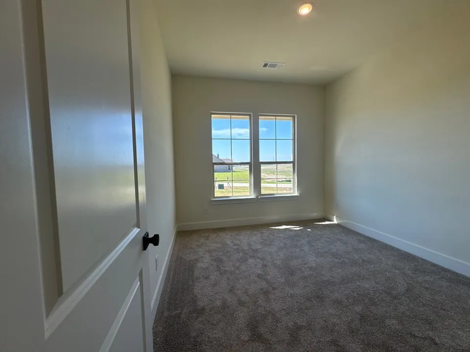 Plush carpet flooring, recessed ceiling lighting, a panel door with matte black hardware, and two large grid windows