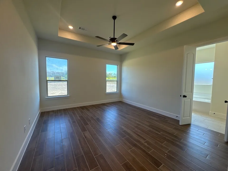 Wood-finish flooring, tray ceiling with recessed lighting, ceiling fan, and two windows