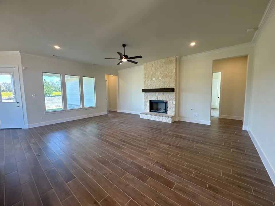 Wood-finish tile flooring throughout, stone-clad fireplace with a wood mantle, three panel windows, ceiling fan with integrated lighting, and recessed lighting
