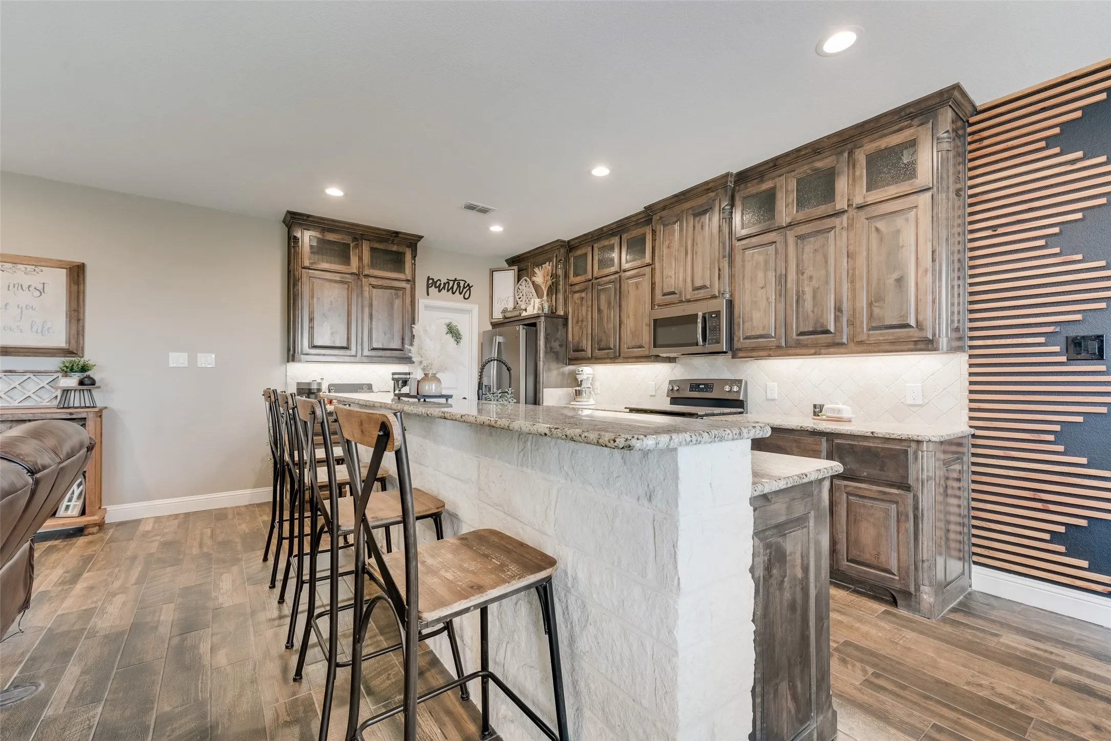 Kitchen featuring a stone-clad island with a granite countertop, wood-finish flooring, recessed lighting, and a patterned accent wall