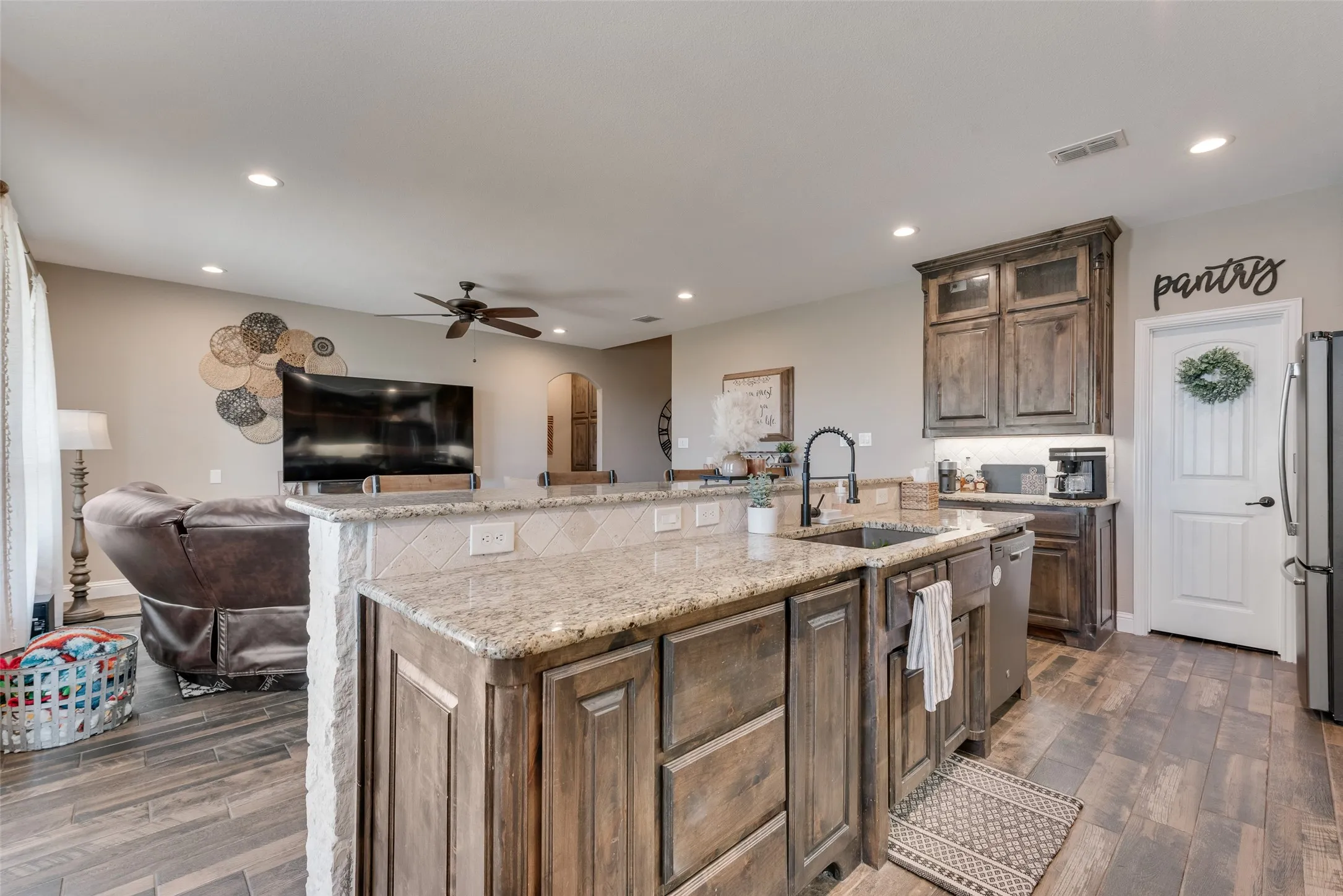 Spacious kitchen featuring a large island with granite countertops, wood-finish flooring, recessed lighting, and dark wood cabinetry