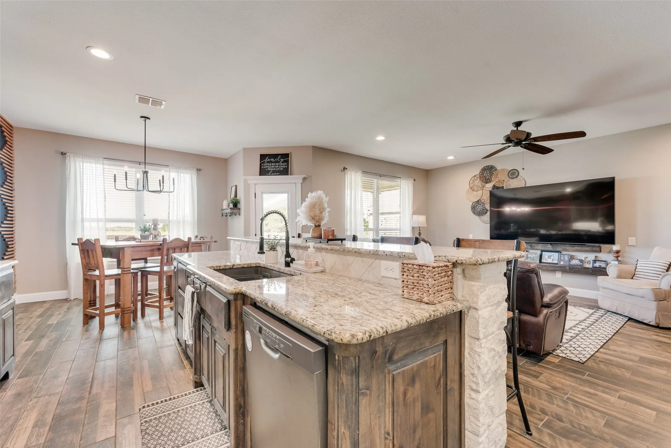 Kitchen island featuring a granite countertop, built-in sink with a gooseneck faucet, and integrated dishwasher