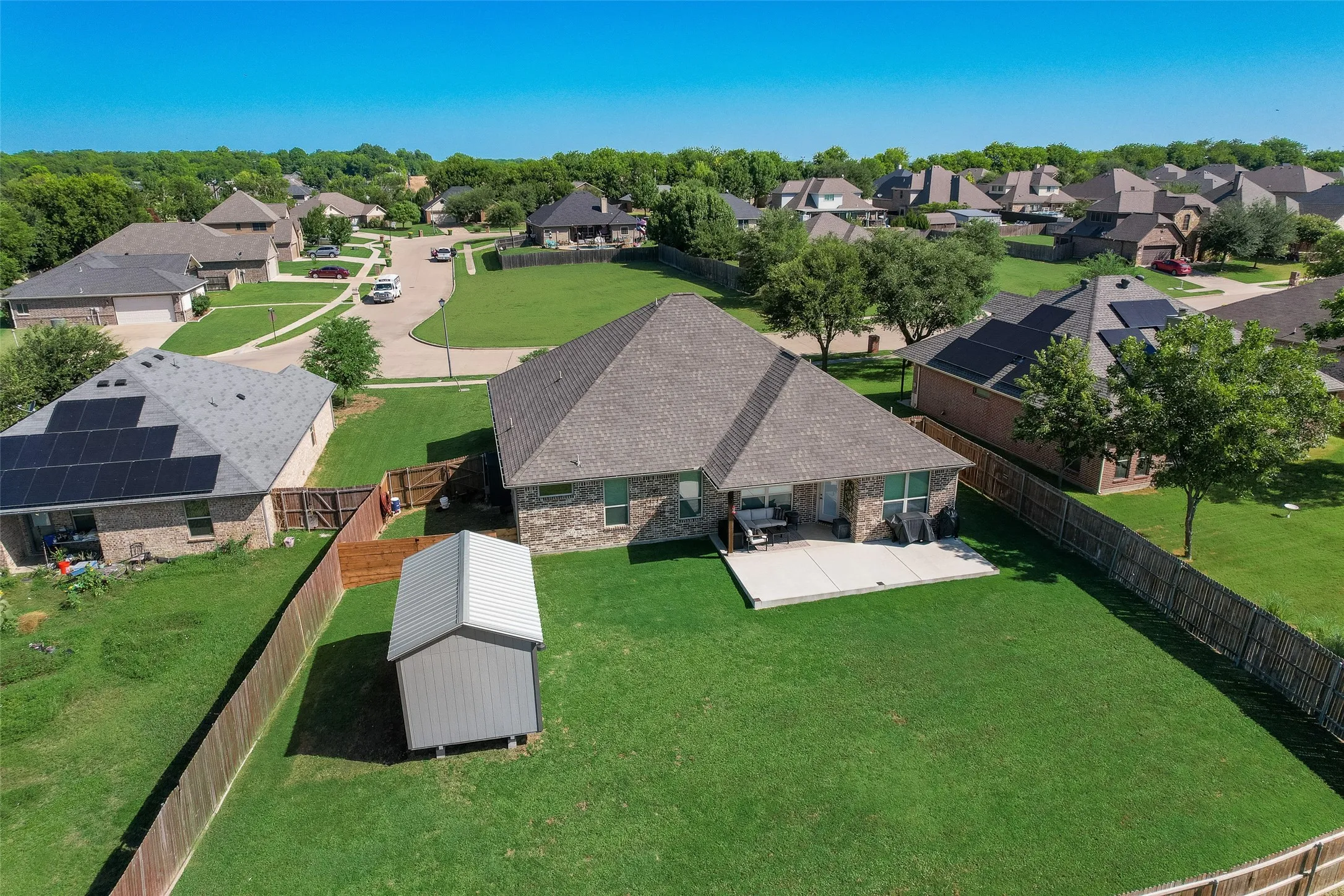 Spacious backyard featuring a manicured lawn, a large concrete patio, and a dedicated storage shed