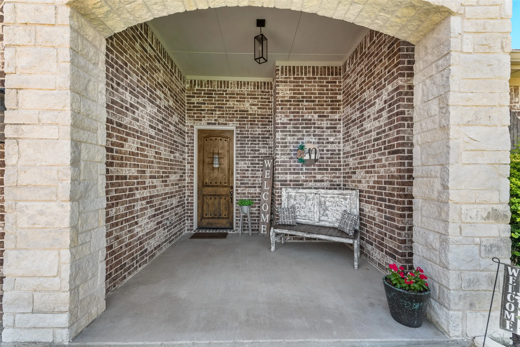 Covered entry featuring a decorative wood door, brick siding, stone archway, and concrete flooring