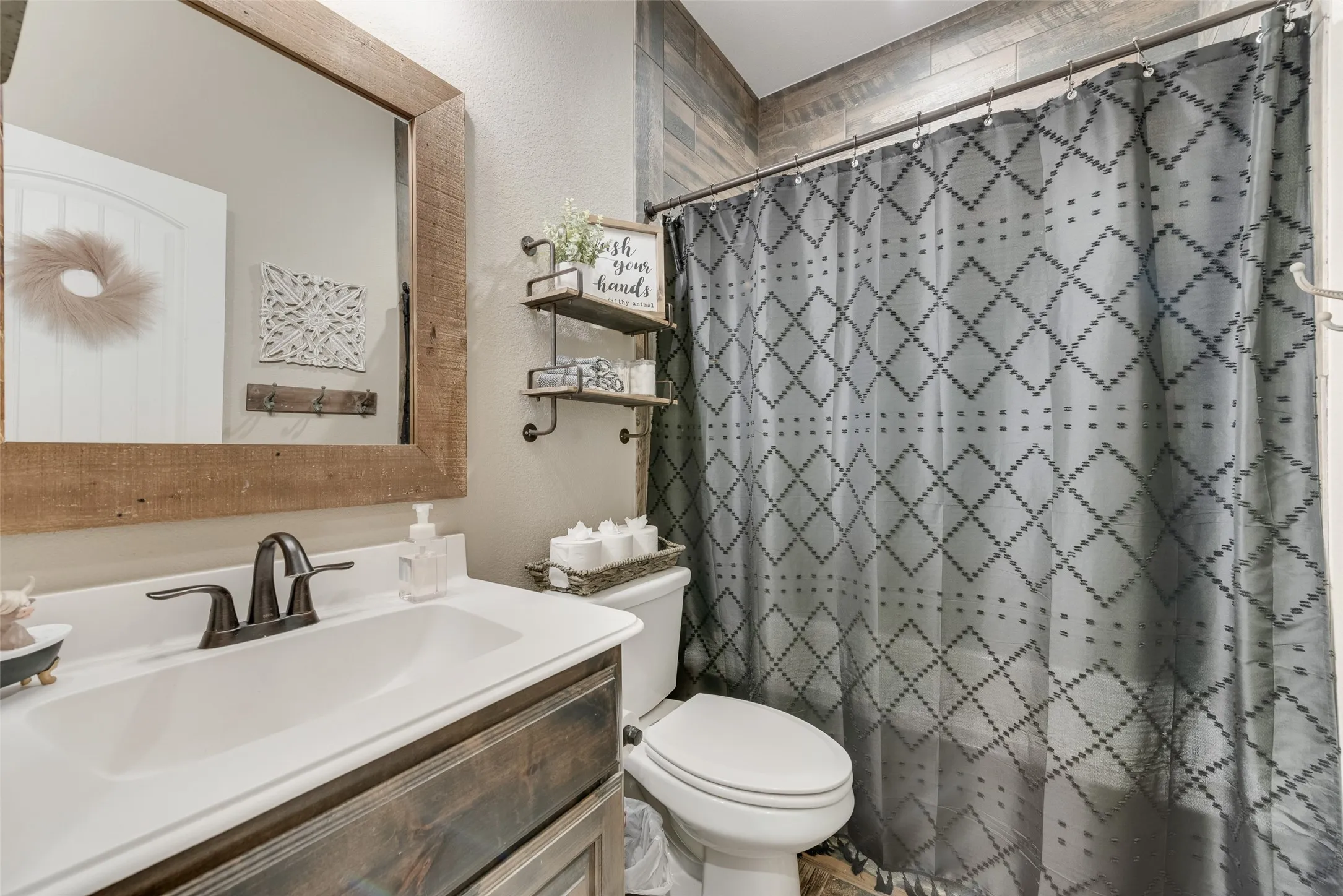 Bathroom featuring a wood-framed mirror, bronze-finish faucet, wood-finish vanity, and a tile shower surround