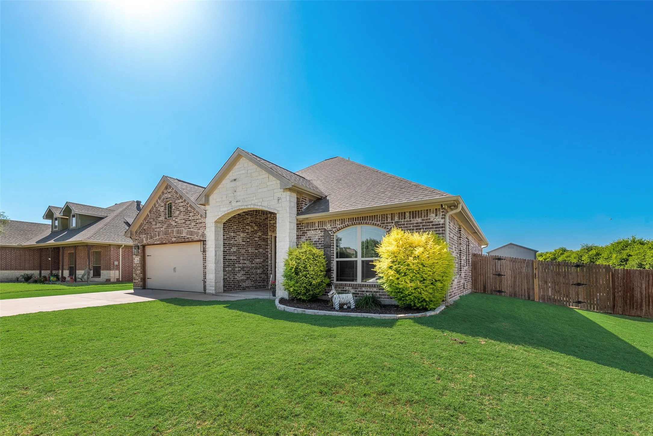 Brick and stone exterior featuring an arched entryway, gabled roofline, front-facing garage, and a fenced backyard