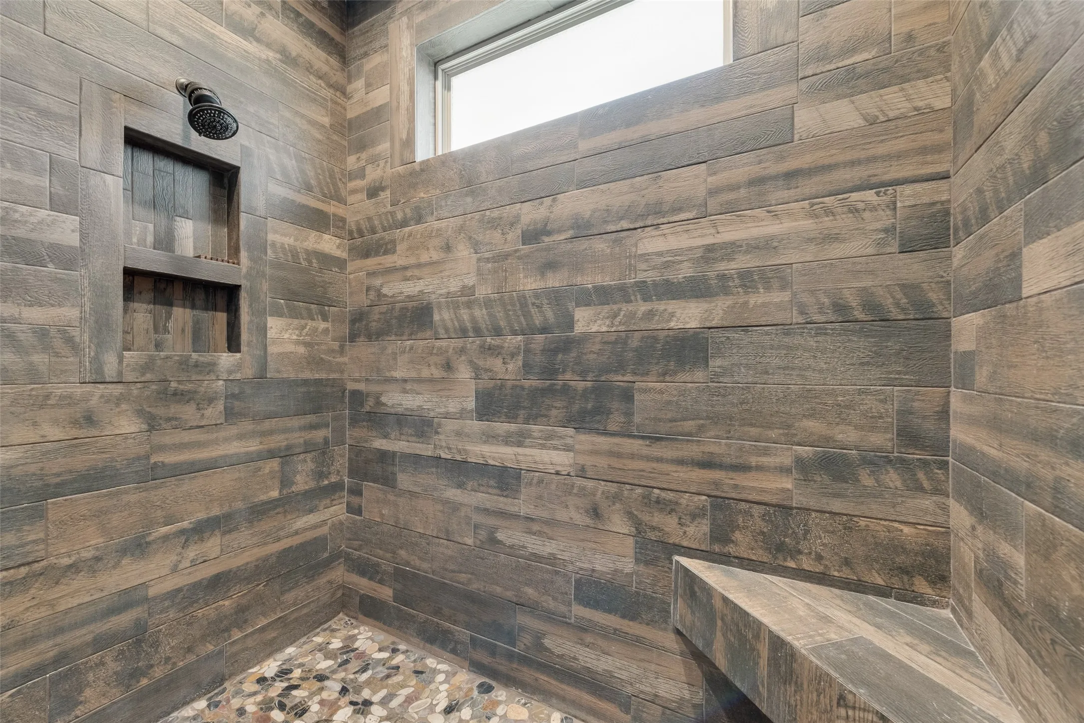 Shower enclosure featuring wood-look tile walls, a built-in shower niche, and a corner bench
