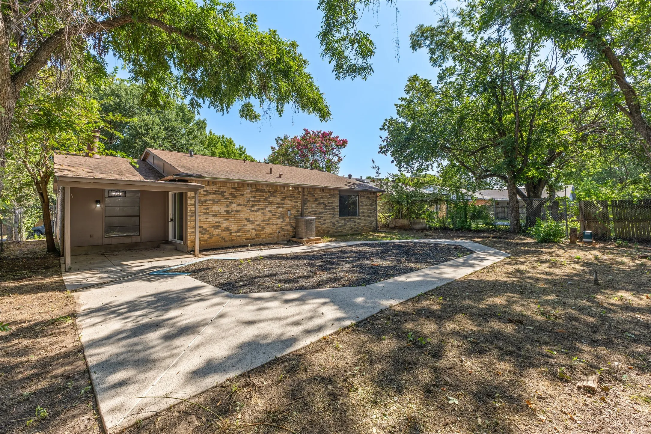Expansive backyard with a concrete patio, brick exterior, and mature trees providing natural shade