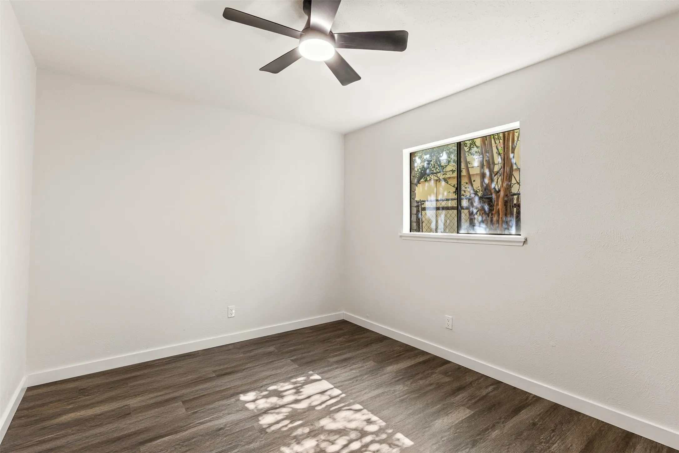 Room featuring wood-finish flooring, crisp white walls, and a contemporary ceiling fan