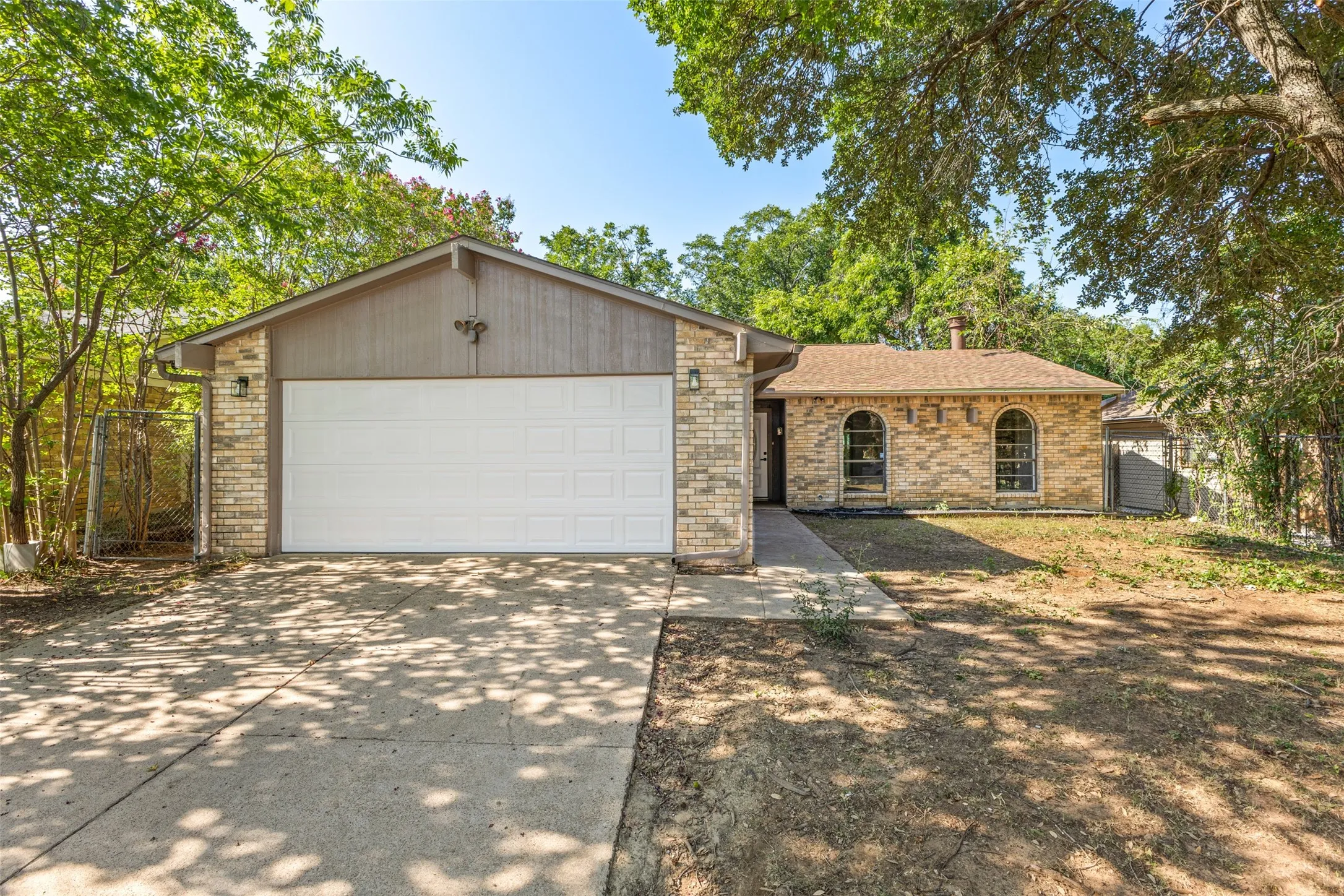 Brick exterior with arched windows, an attached garage, and a concrete driveway