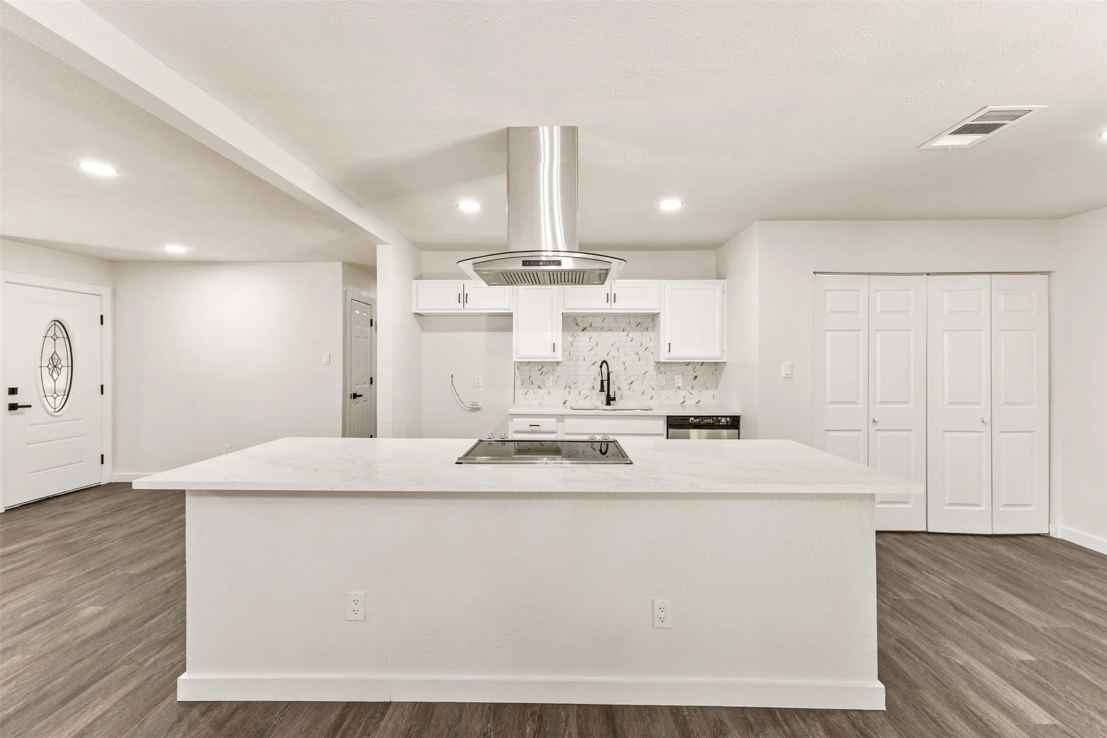 Modern kitchen with an expansive island featuring an integrated cooktop and a sleek stainless steel range hood