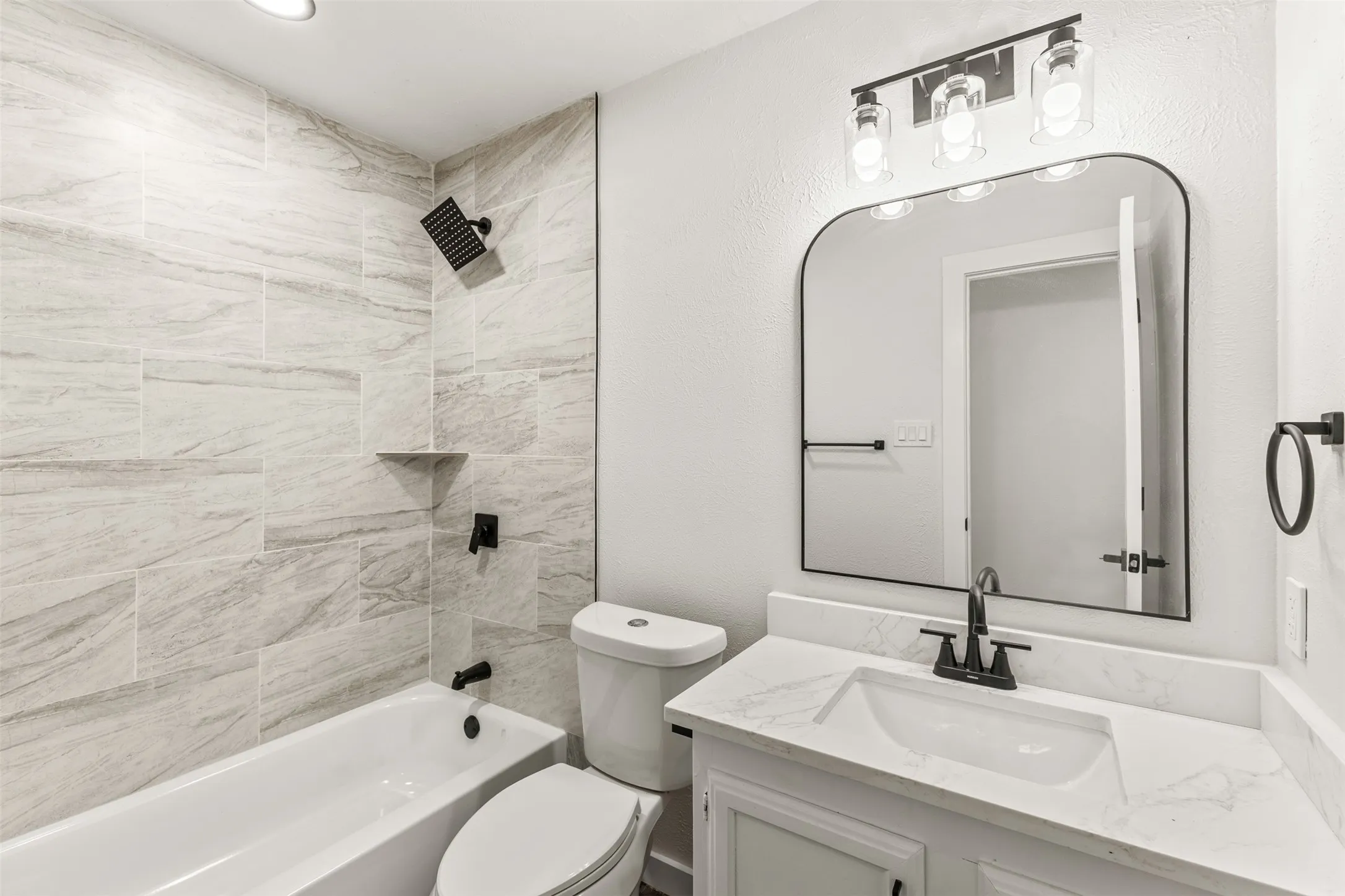 Bathroom featuring a white bathtub, light-toned tiled shower surround with a built-in corner shelf, and a white vanity with a light-colored countertop