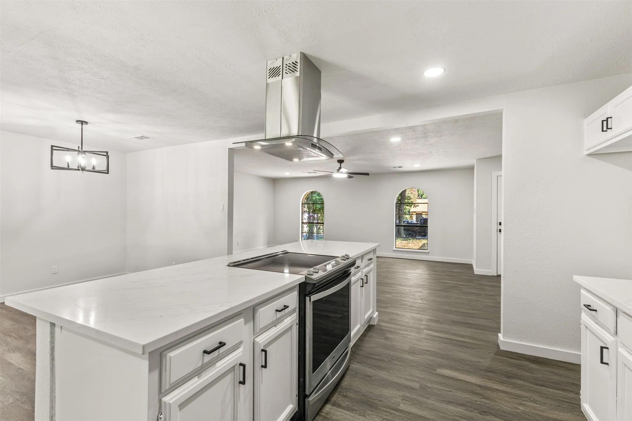 Kitchen island with integrated range and stainless steel hood, white cabinetry with black hardware, wood-finish flooring, and arched windows