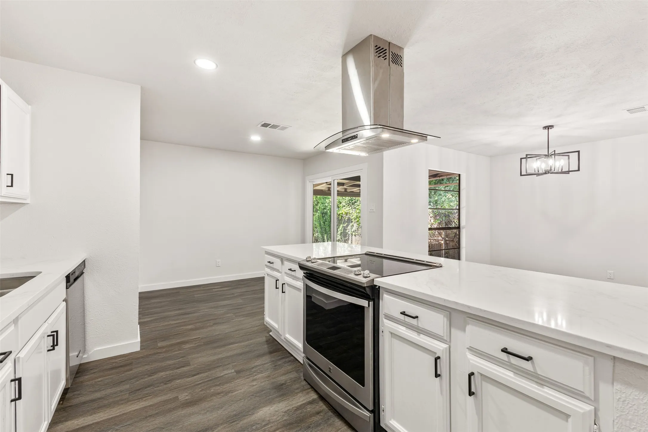 Kitchen featuring a large island with an integrated cooktop and stainless steel oven, white cabinetry, light-toned countertops, and wood-finish flooring