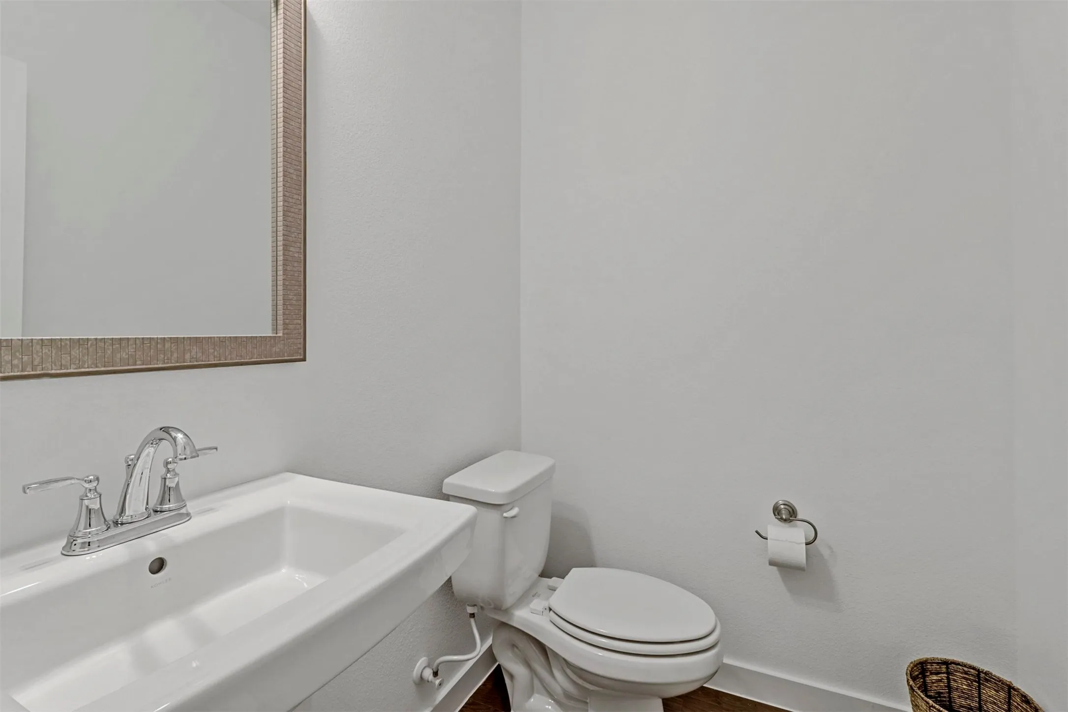 Powder room featuring a pedestal sink, chrome faucet, framed mirror, and white toilet