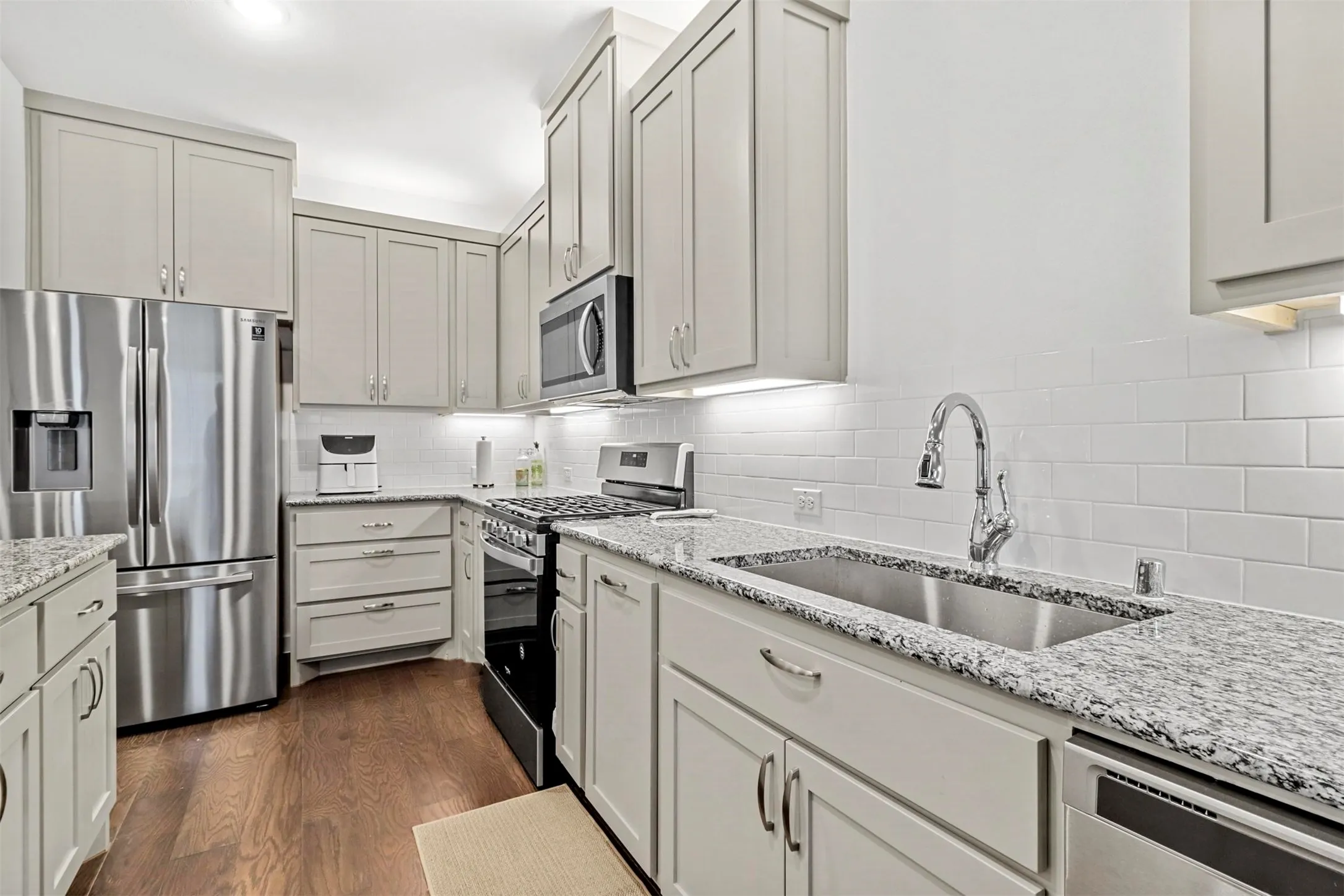 Modern kitchen featuring light cabinetry, granite countertops, subway tile backsplash, stainless steel appliances, and wood-finish flooring