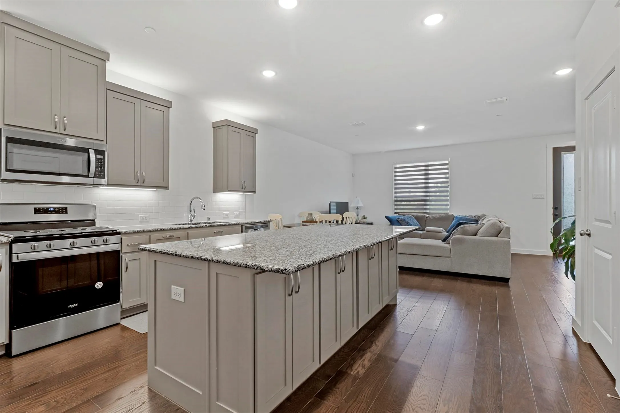 Kitchen featuring an expansive island with a granite countertop, light gray cabinetry, stainless steel appliances, and wood-finish flooring