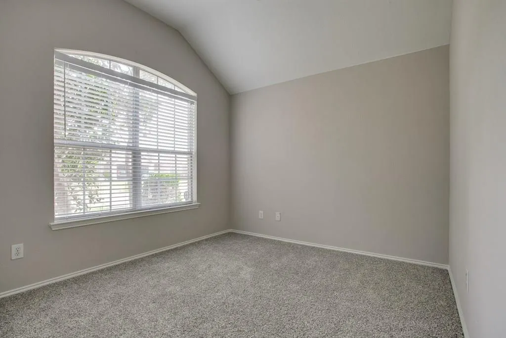 Arched window with horizontal blinds, sloped ceiling, light gray wall paint, white baseboards, and gray speckled carpeting