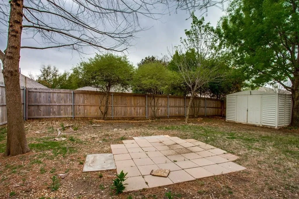 Spacious backyard featuring a wood privacy fence, established trees, a paver patio area, and a white storage shed