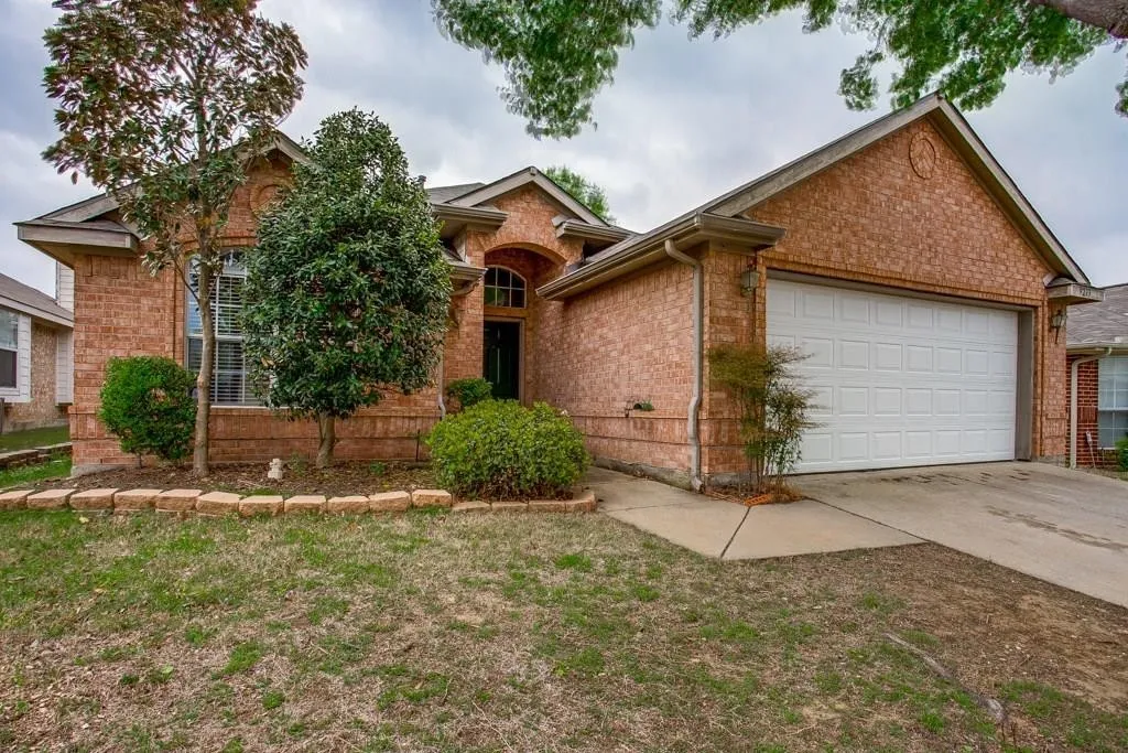 Brick facade residence featuring an arched entry, an attached garage, a paved driveway, and mature landscaping