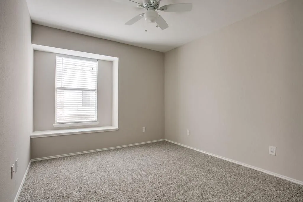 Spacious room featuring neutral paint, light gray carpeting, a window with horizontal blinds, and a ceiling fan