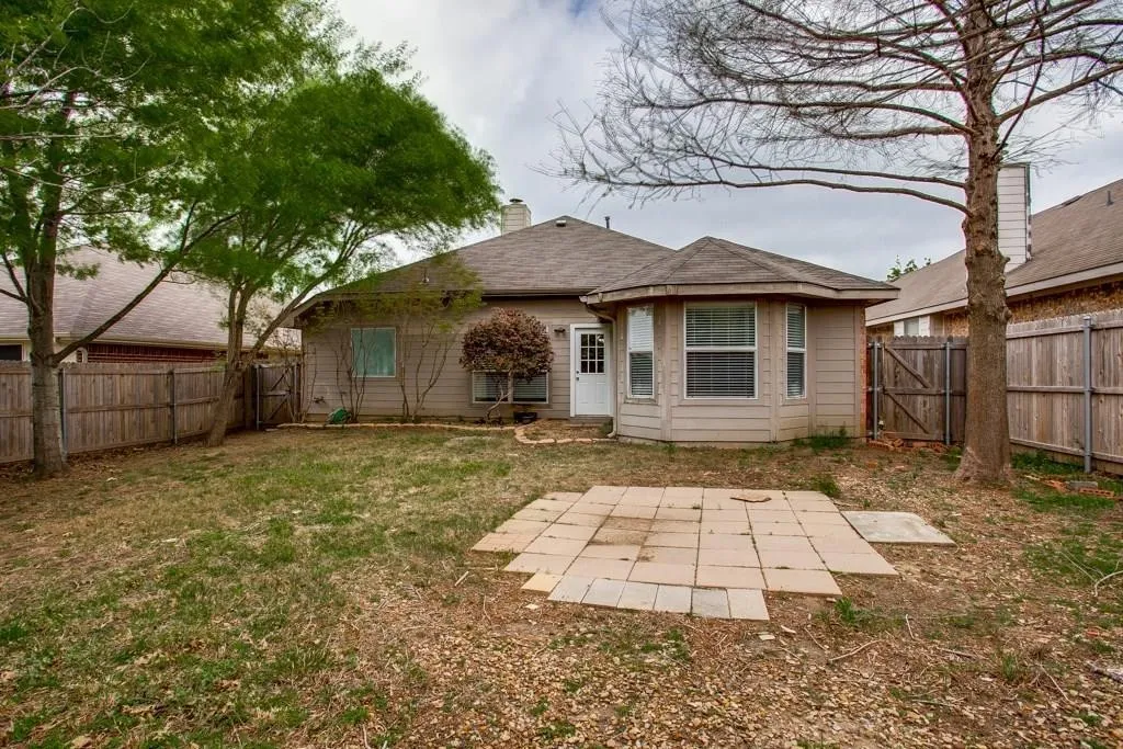 Expansive backyard featuring a stone paver patio, mature trees, and privacy fencing