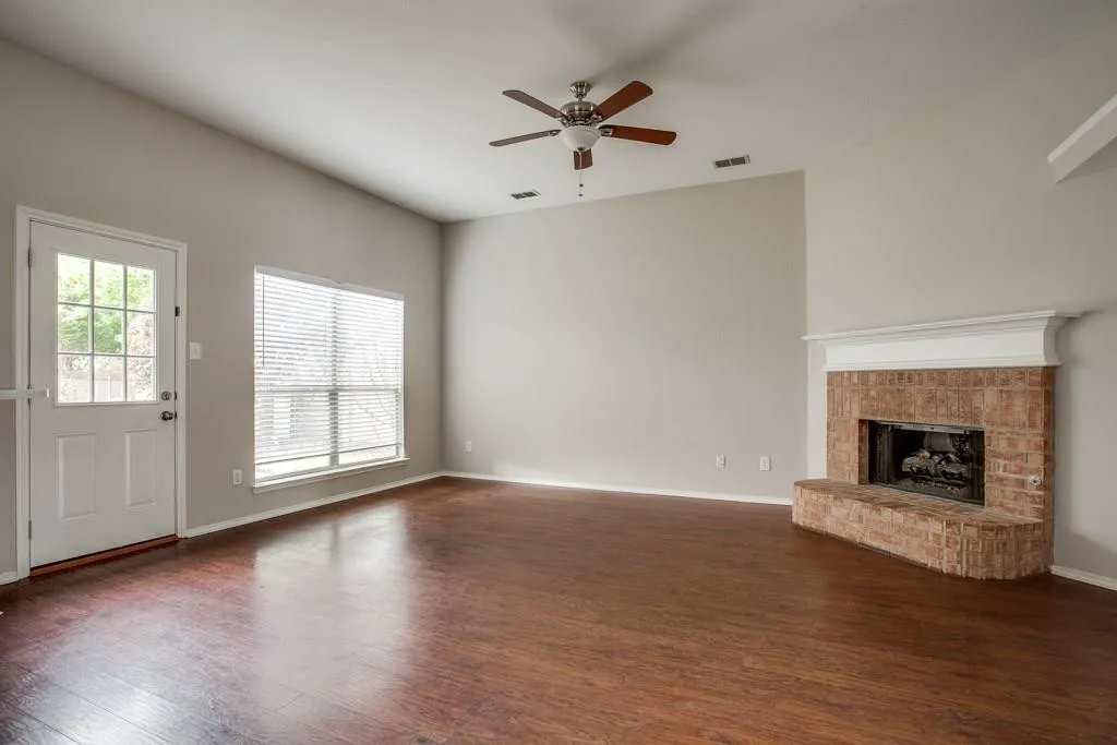 Spacious living area featuring wood-finish flooring, a brick fireplace with a white mantel, and a multi-pane glass-insert door