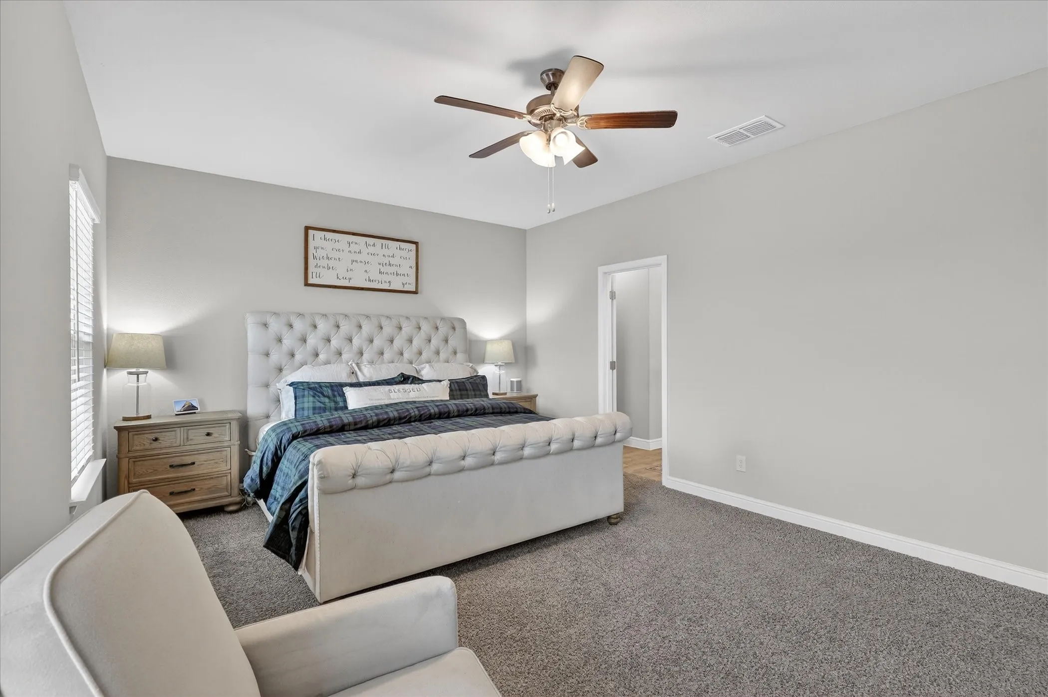 Spacious interior featuring a neutral color palette, ceiling fan with integrated lighting, window with blinds, and durable carpeting