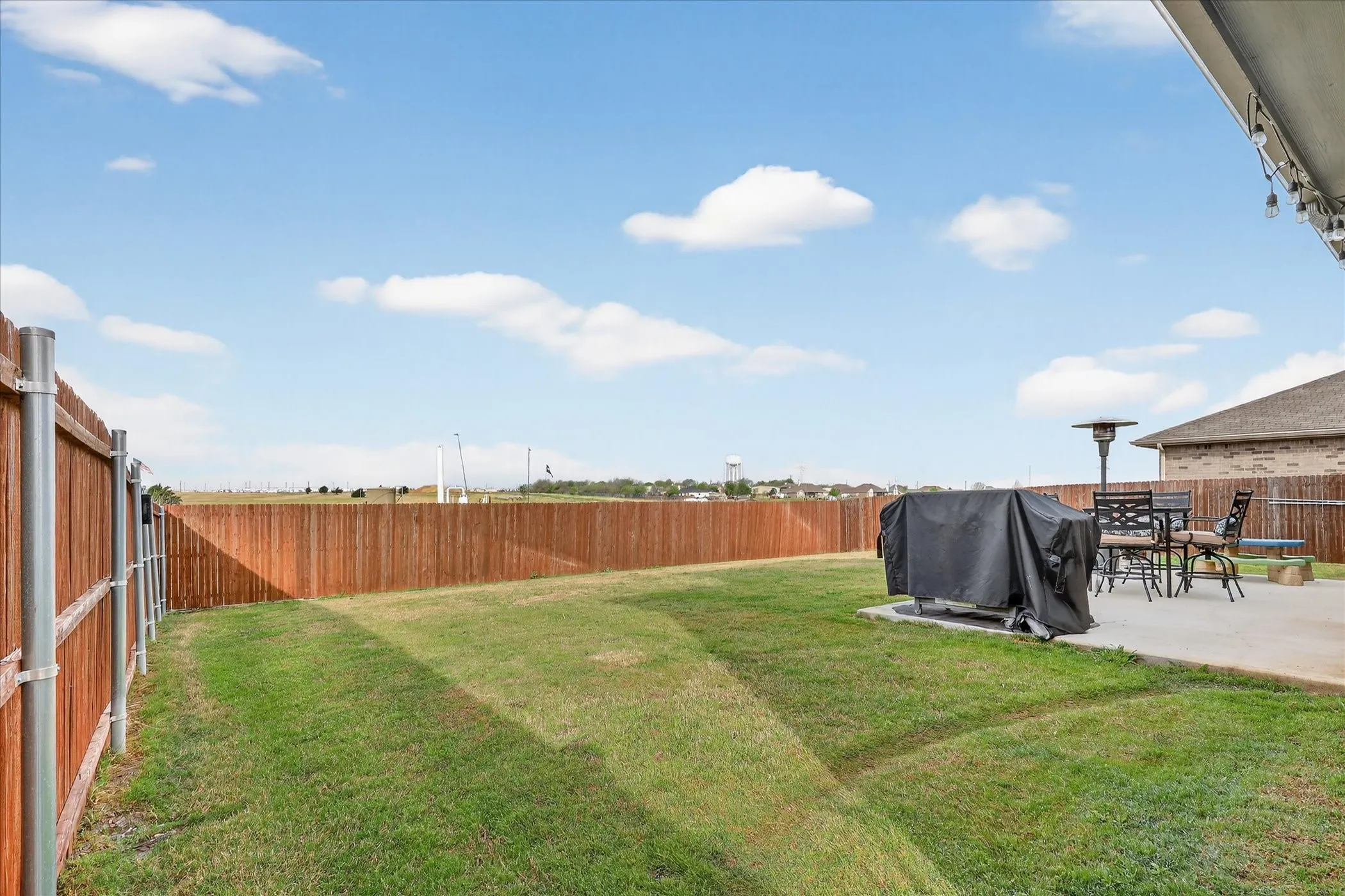 Expansive backyard featuring a manicured lawn, a full wood privacy fence, and a concrete patio