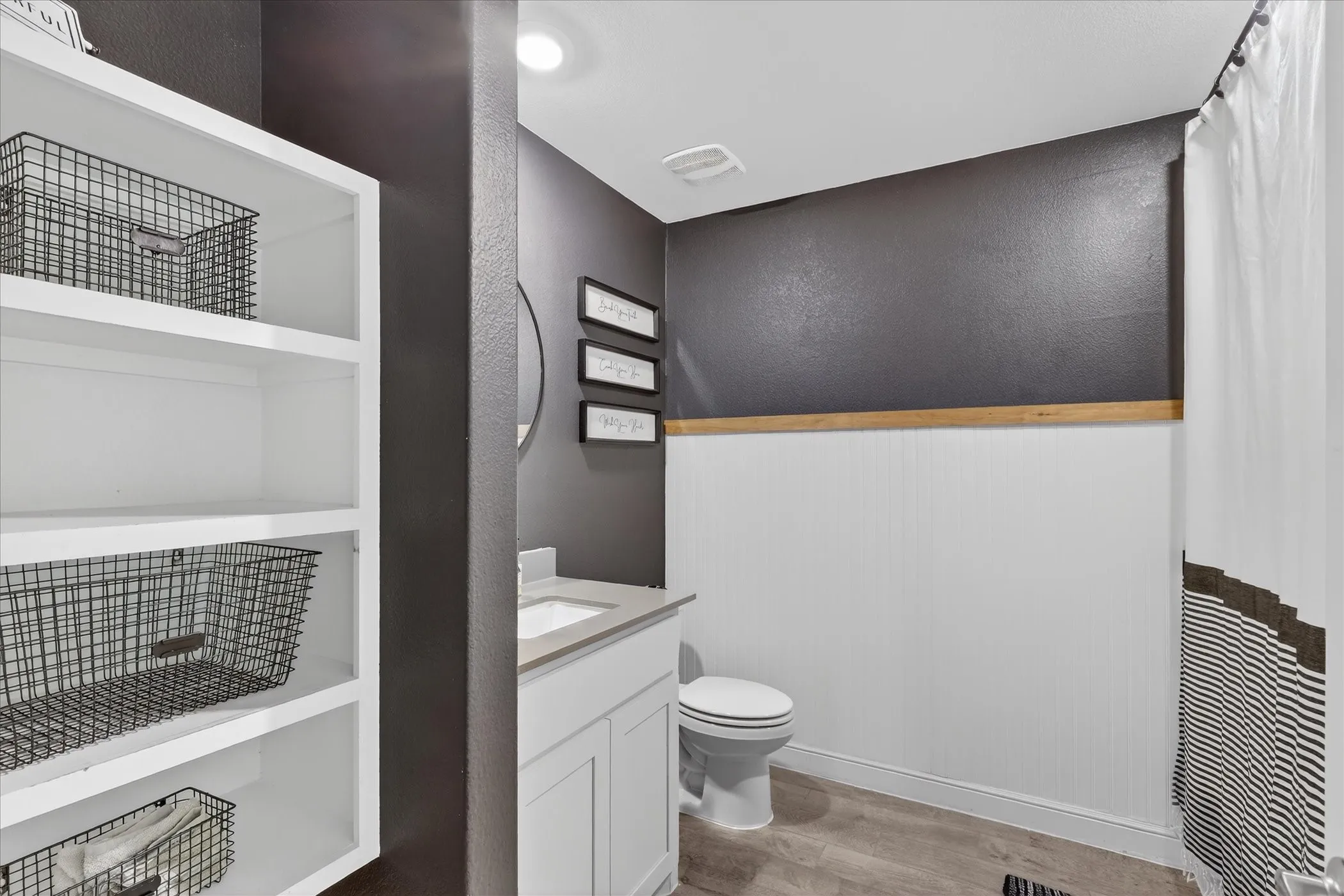 Bathroom featuring a built-in white shelving unit, a white vanity with an undermount sink, a toilet, a full shower with a white curtain, and wood-finish flooring