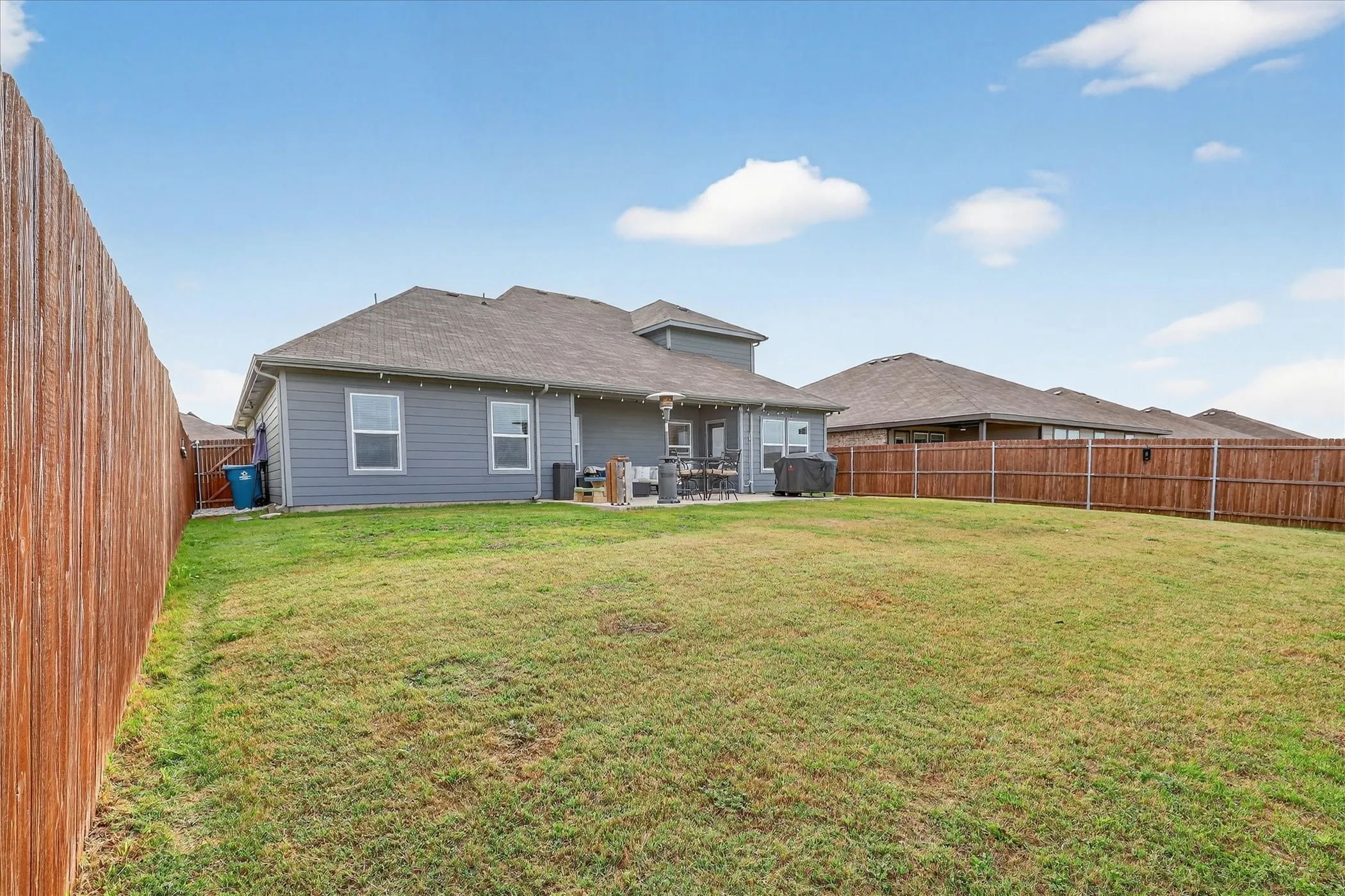Expansive backyard featuring a lush lawn, privacy fencing, and a concrete patio