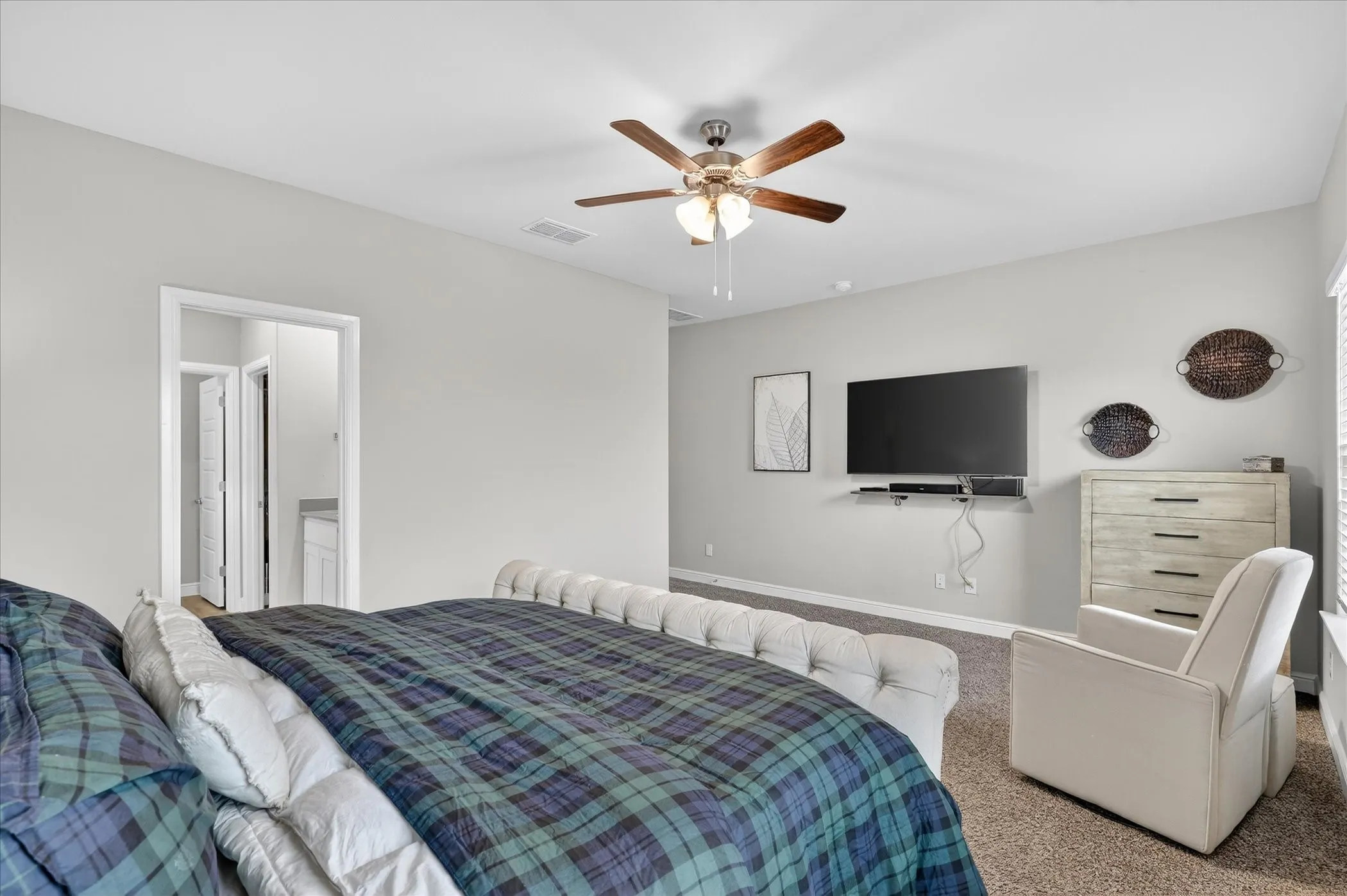 Spacious bedroom featuring light neutral wall tones, carpeted flooring, and a ceiling fan with integrated lighting
