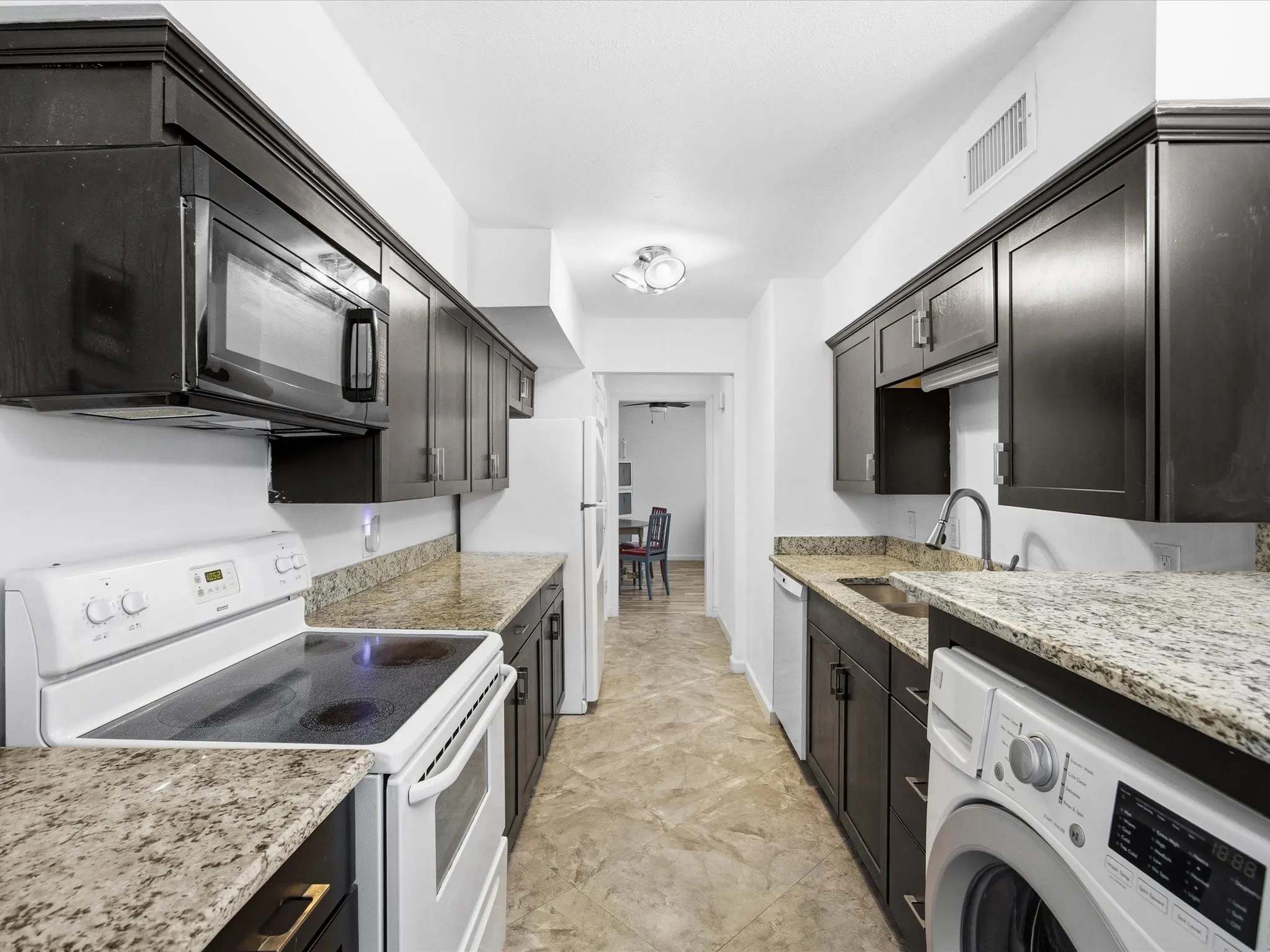 Kitchen with white appliances, washer / dryer, and light stone countertops