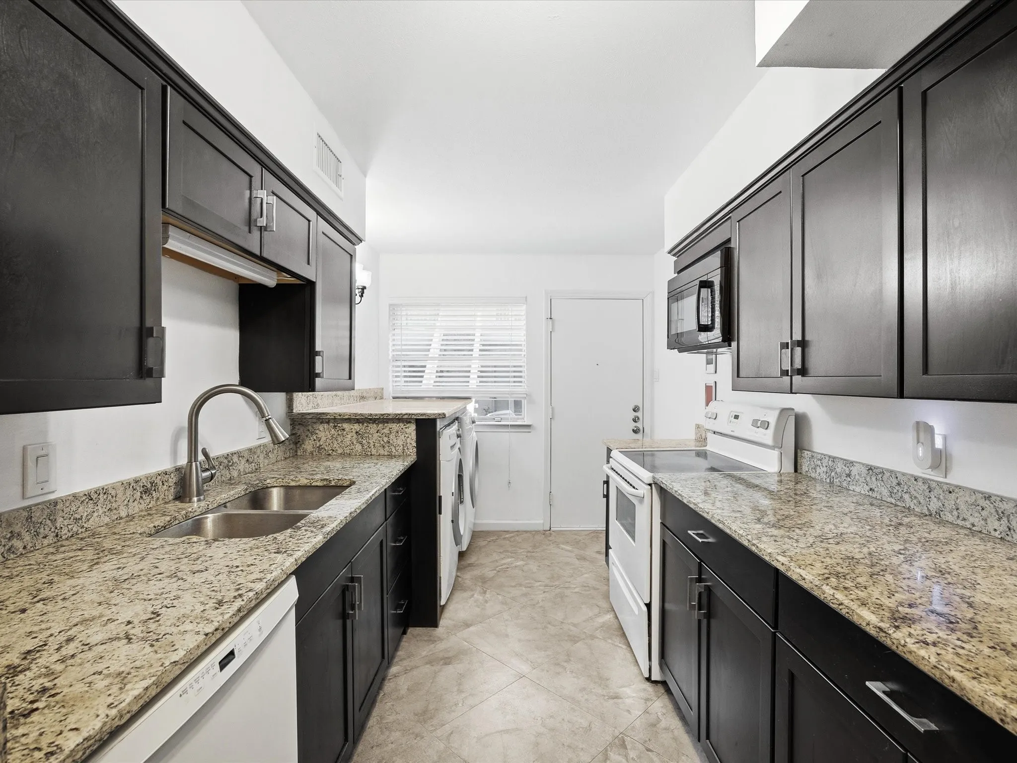 Kitchen featuring white appliances, light stone countertops, and dark cabinetry