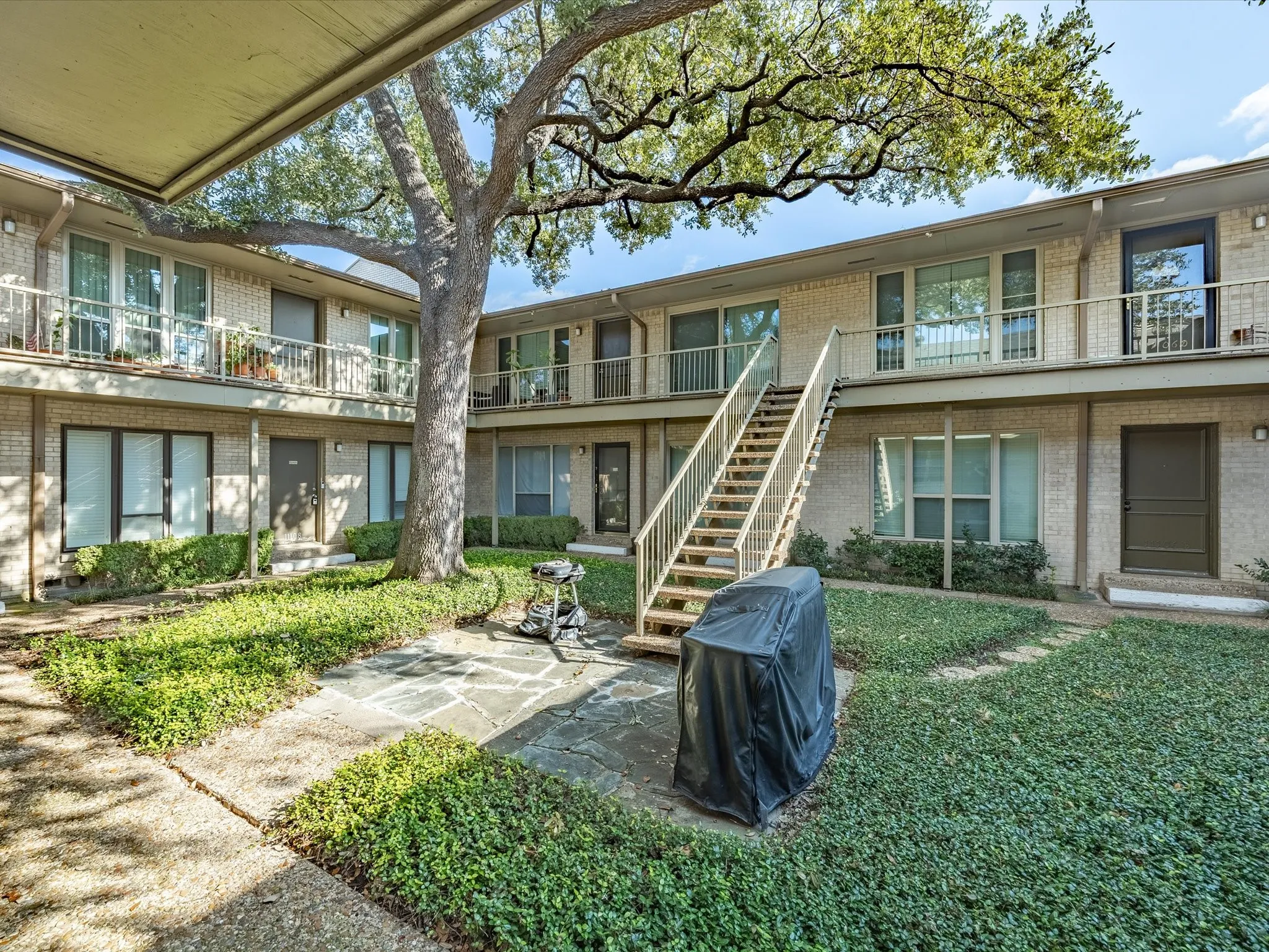 Rear view of house featuring stairs, a balcony, brick siding, and a lawn