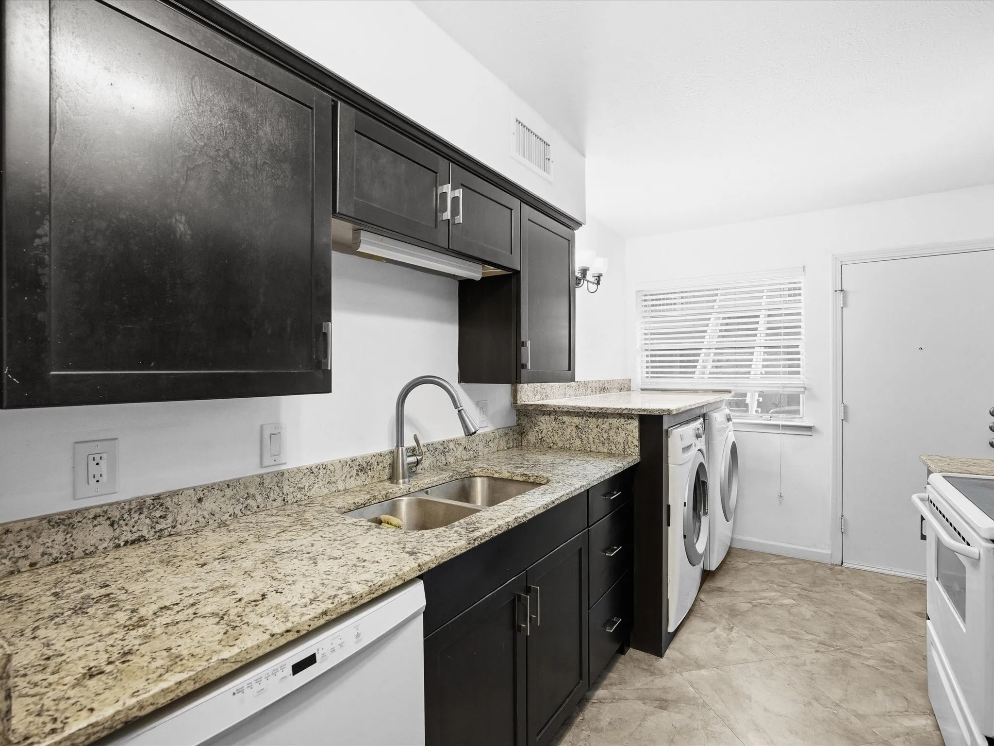 Kitchen featuring light stone counters, dark cabinets, white appliances, and washer and dryer