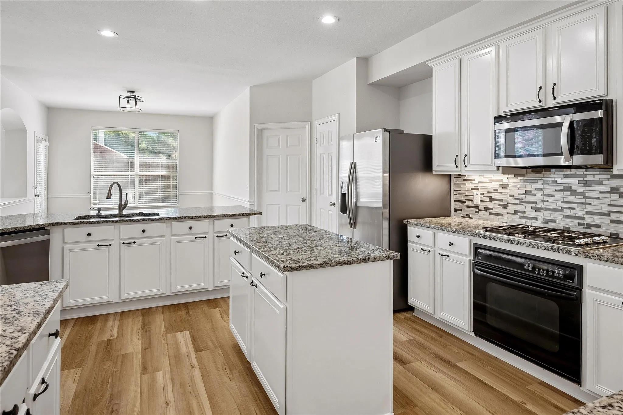 Modern kitchen featuring wood-finish flooring, white cabinetry, speckled countertops, a mosaic tile backsplash, and stainless steel appliances