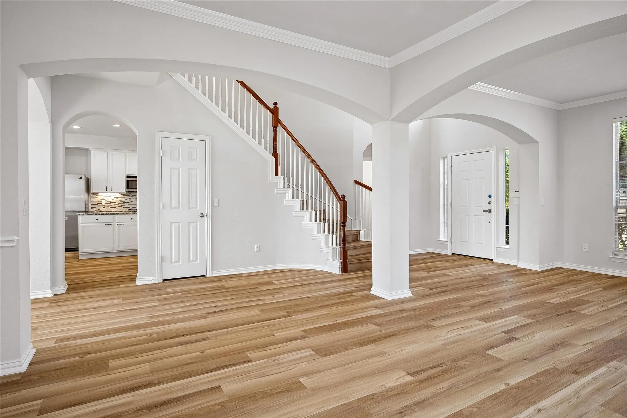 FORMAL DINING ROOM - Entryway featuring wood-finish flooring, a white staircase with wood handrails, arched doorways, a paneled front door with sidelights, and white trim throughout