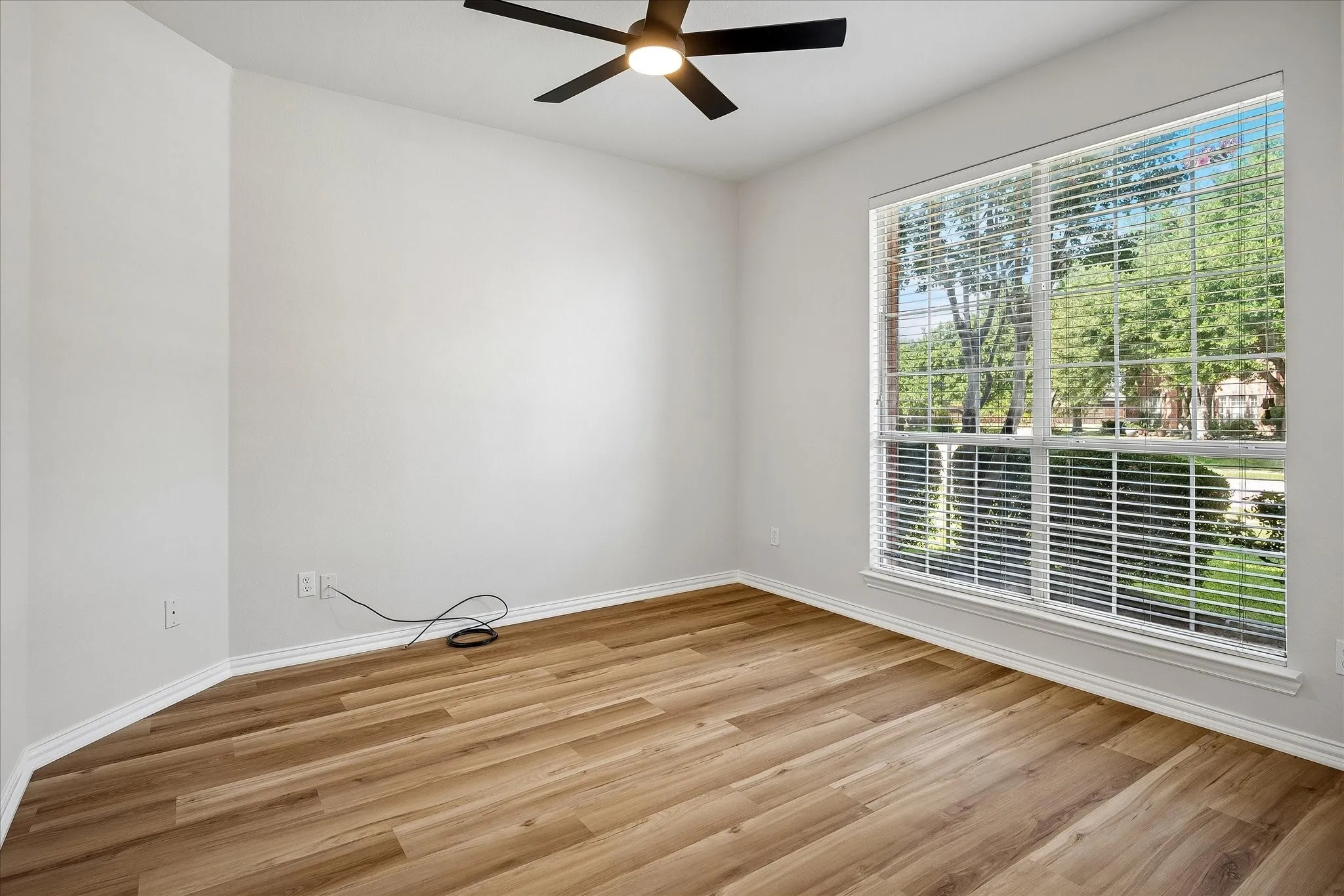 Spacious room featuring wood-finish flooring, a large window with horizontal blinds, and a ceiling fan
