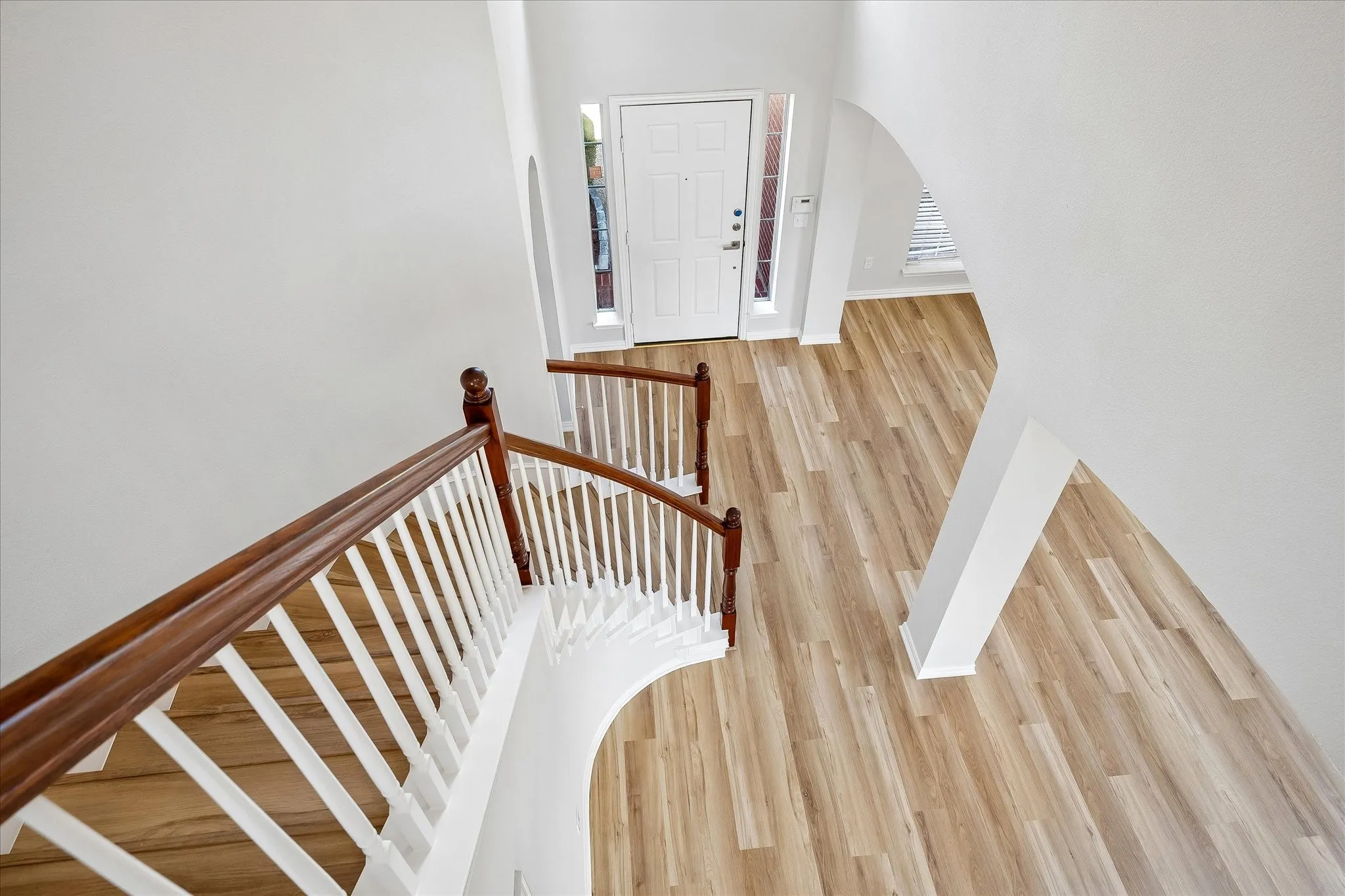 Spacious entryway featuring wood-finish flooring, a white front door with sidelight windows, and a curved staircase with a wood handrail and white balusters