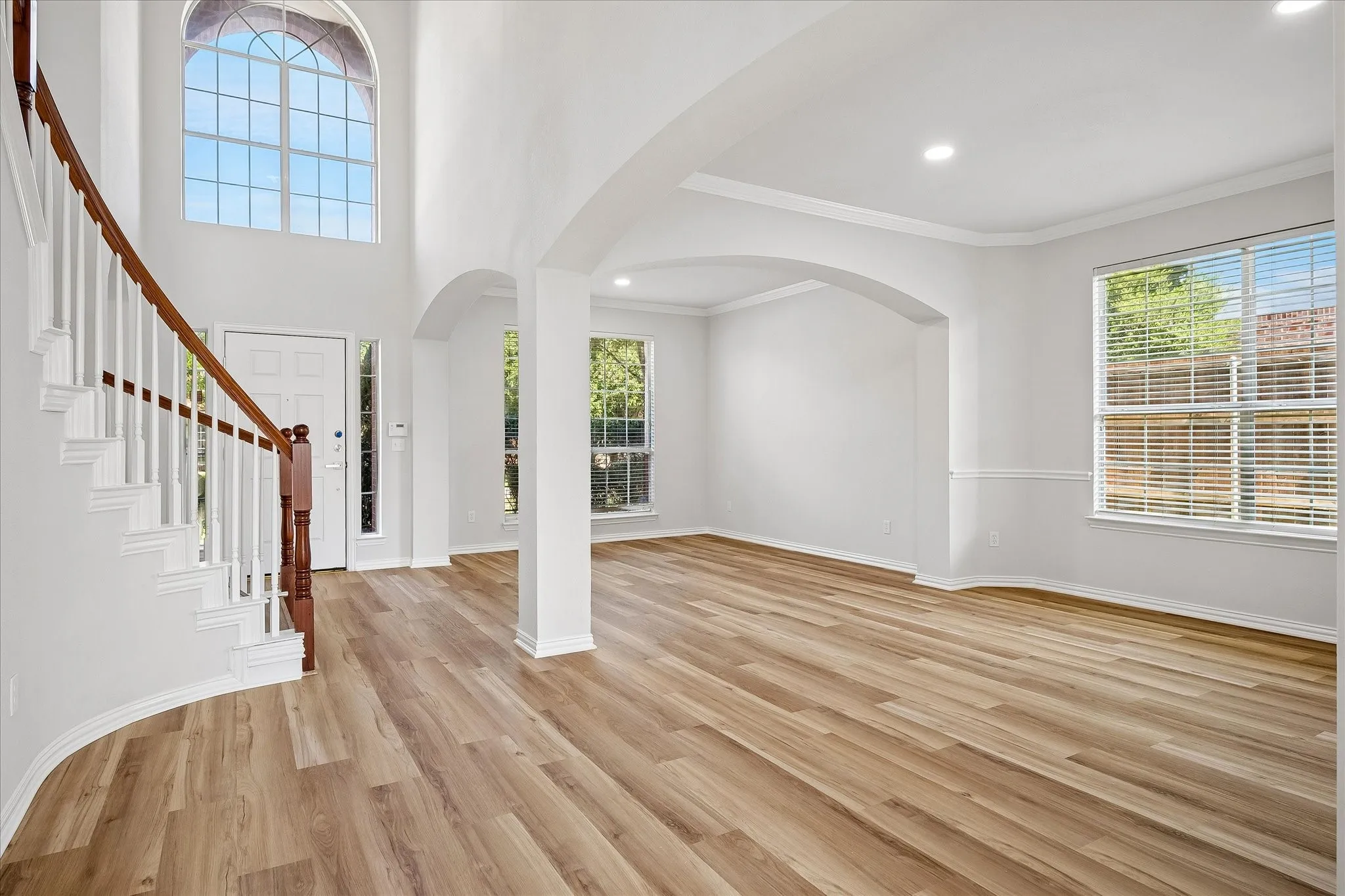 Two-story entry featuring an arched window, wood-finish flooring, and a curved staircase with white balusters