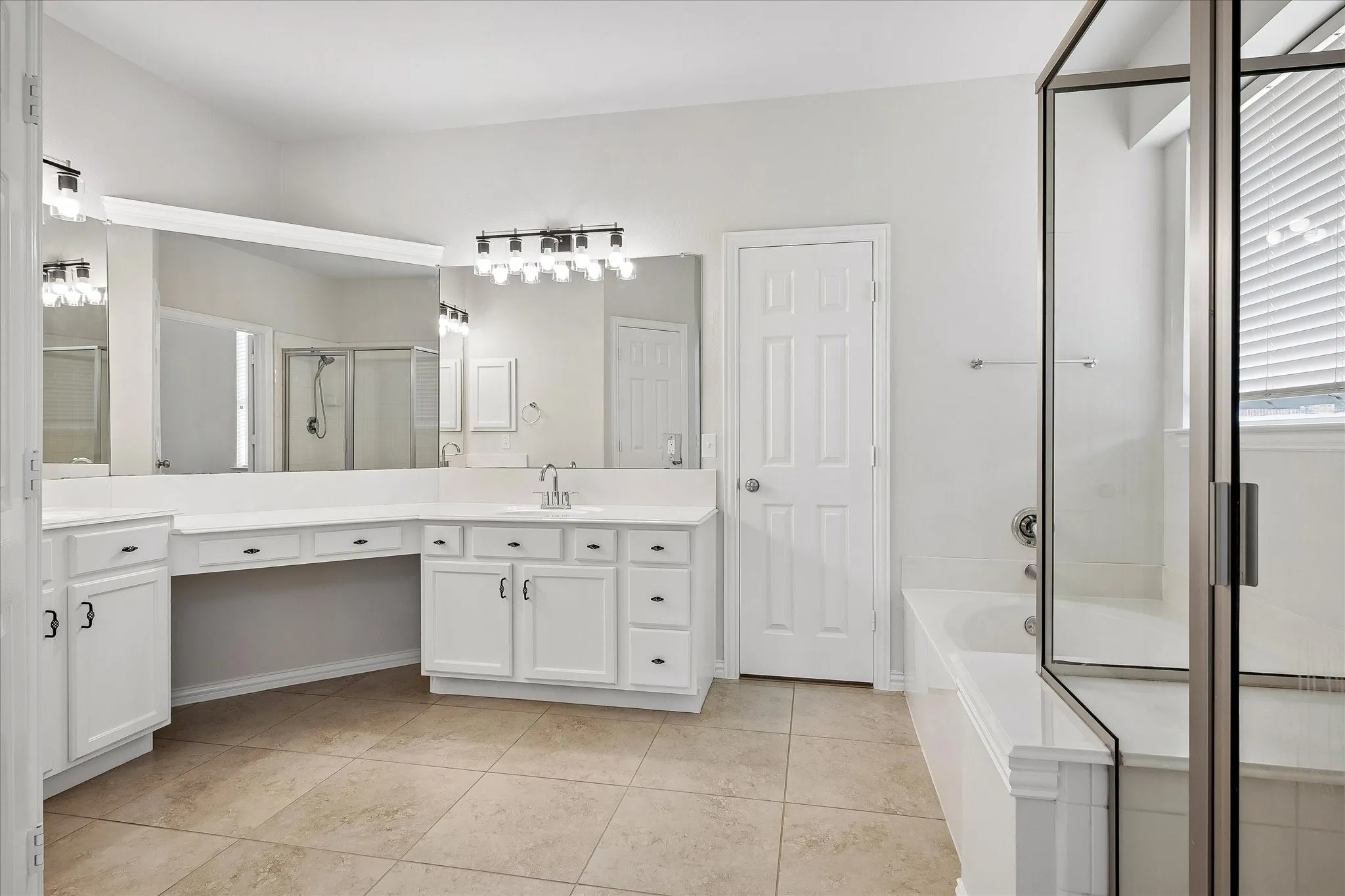 Spacious bathroom featuring a dual vanity with white cabinetry, a built-in makeup counter, and a large wall-mounted mirror