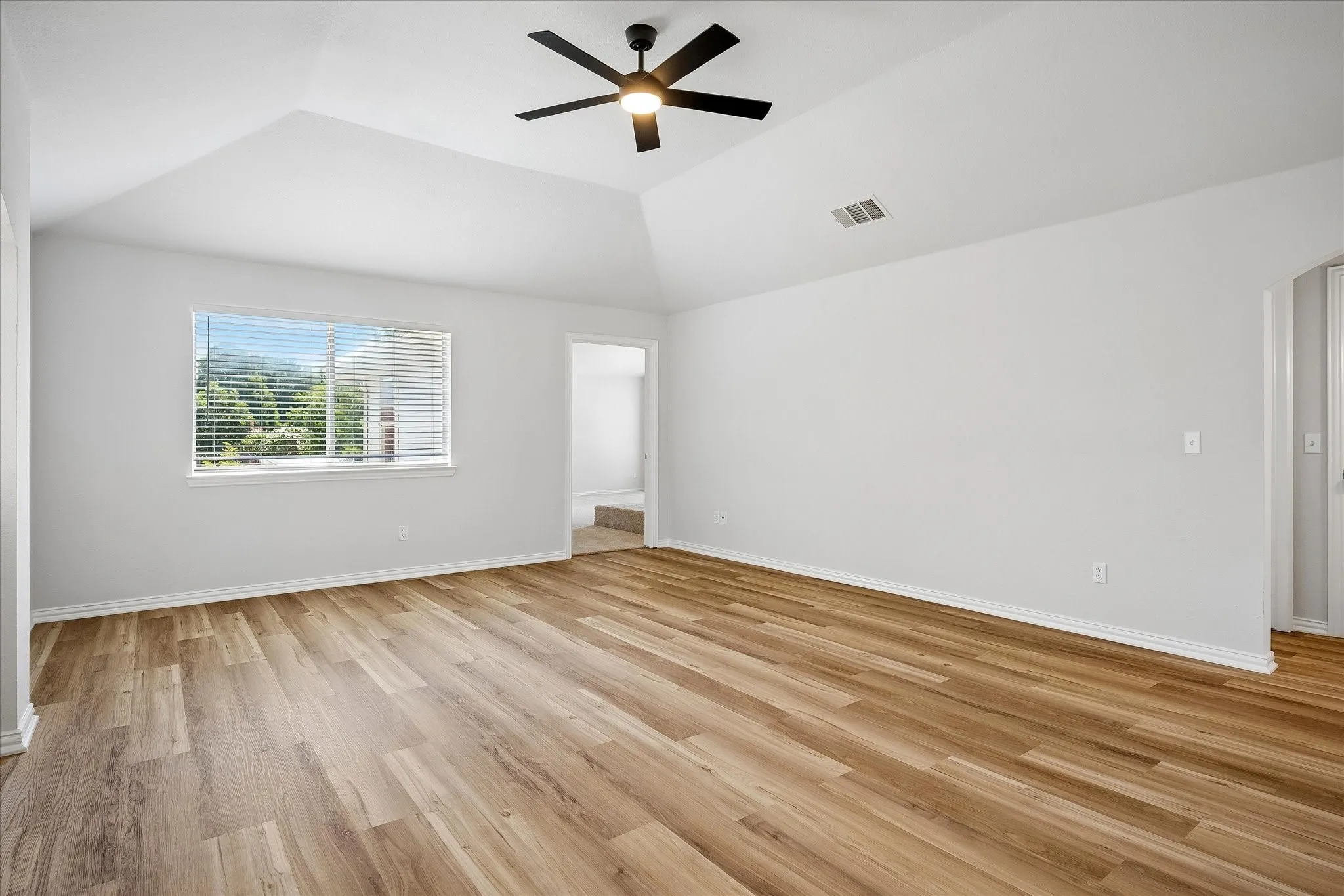 Room with vaulted ceiling, arched window, and neutral carpeting