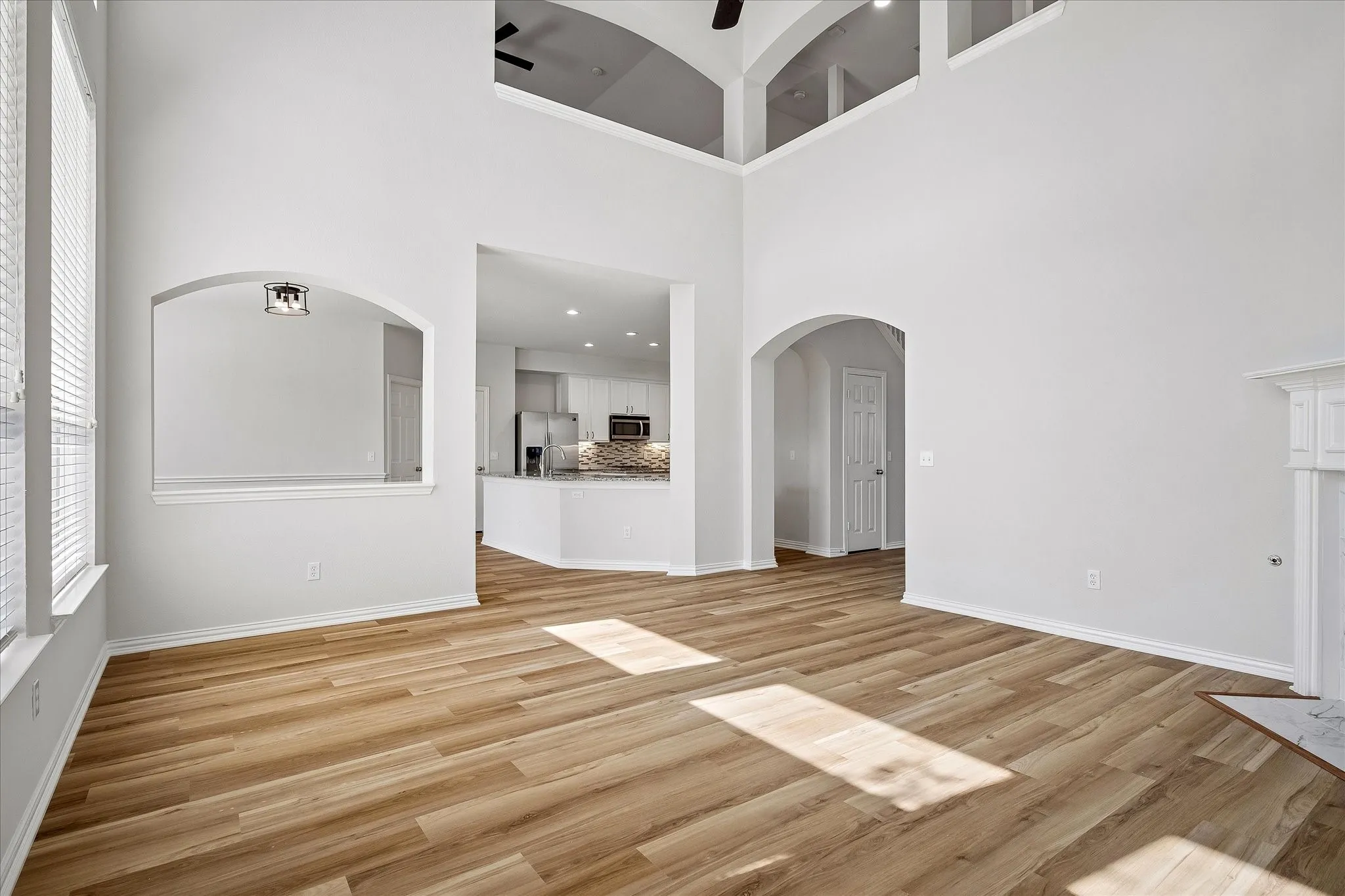 Spacious living area featuring wood-finish flooring, vaulted ceilings, and an open concept layout with arched pass-throughs