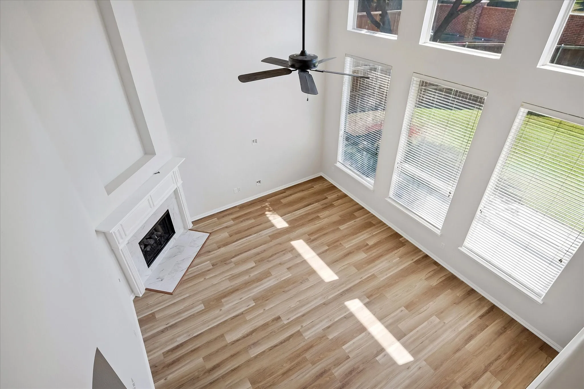 Living area featuring high ceilings, wood-finish flooring, a white mantel fireplace with a dark hearth, multiple windows with blinds, and a ceiling fan